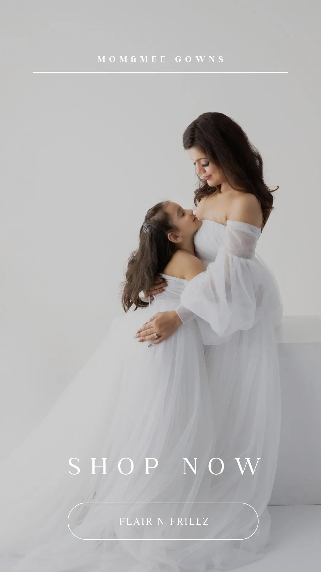 Mother and daughter in matching white maternity gowns, posing together in a bright studio.