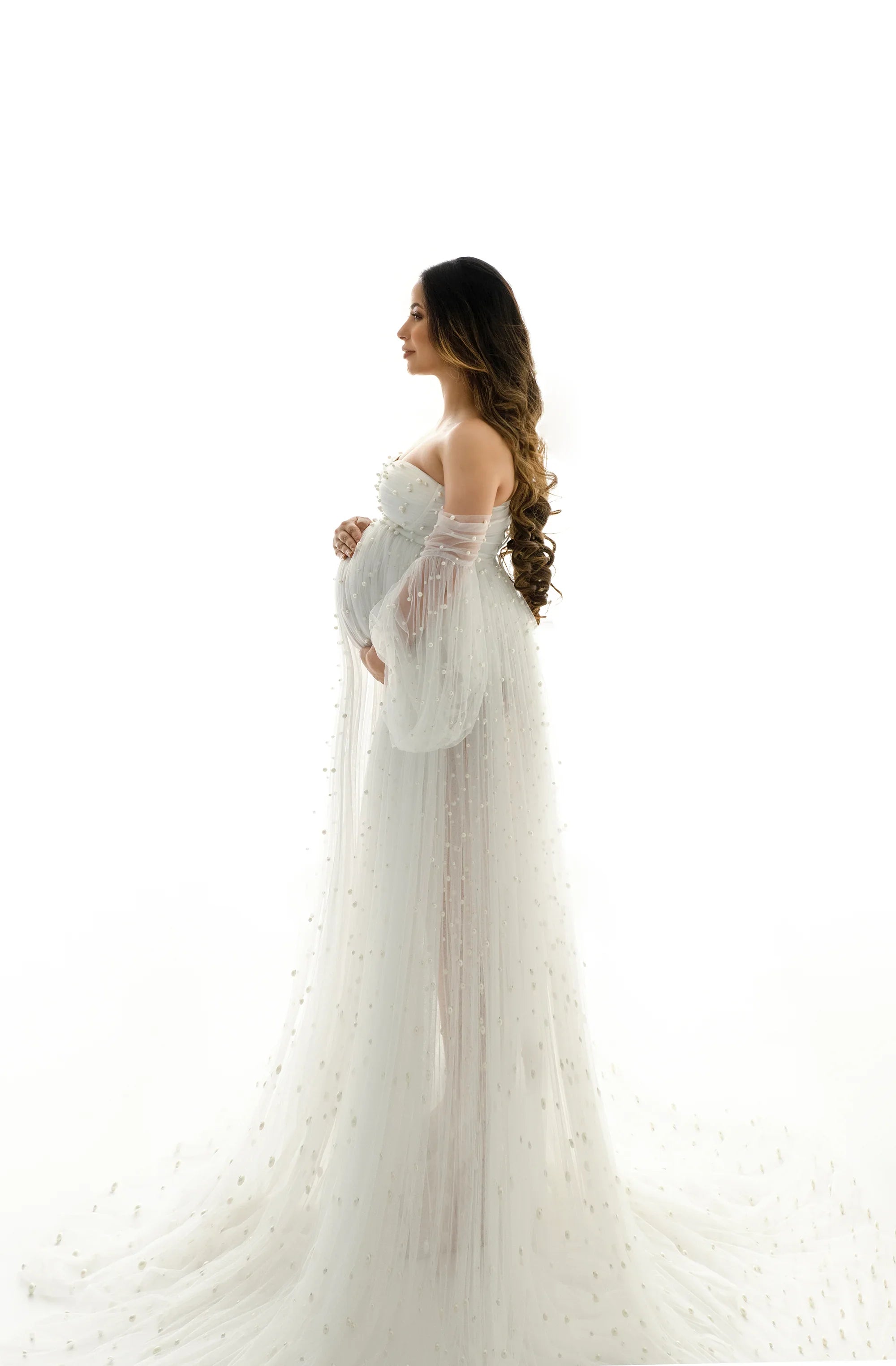 Pregnant woman in elegant white sheer maternity gown with pearl accents, studio light