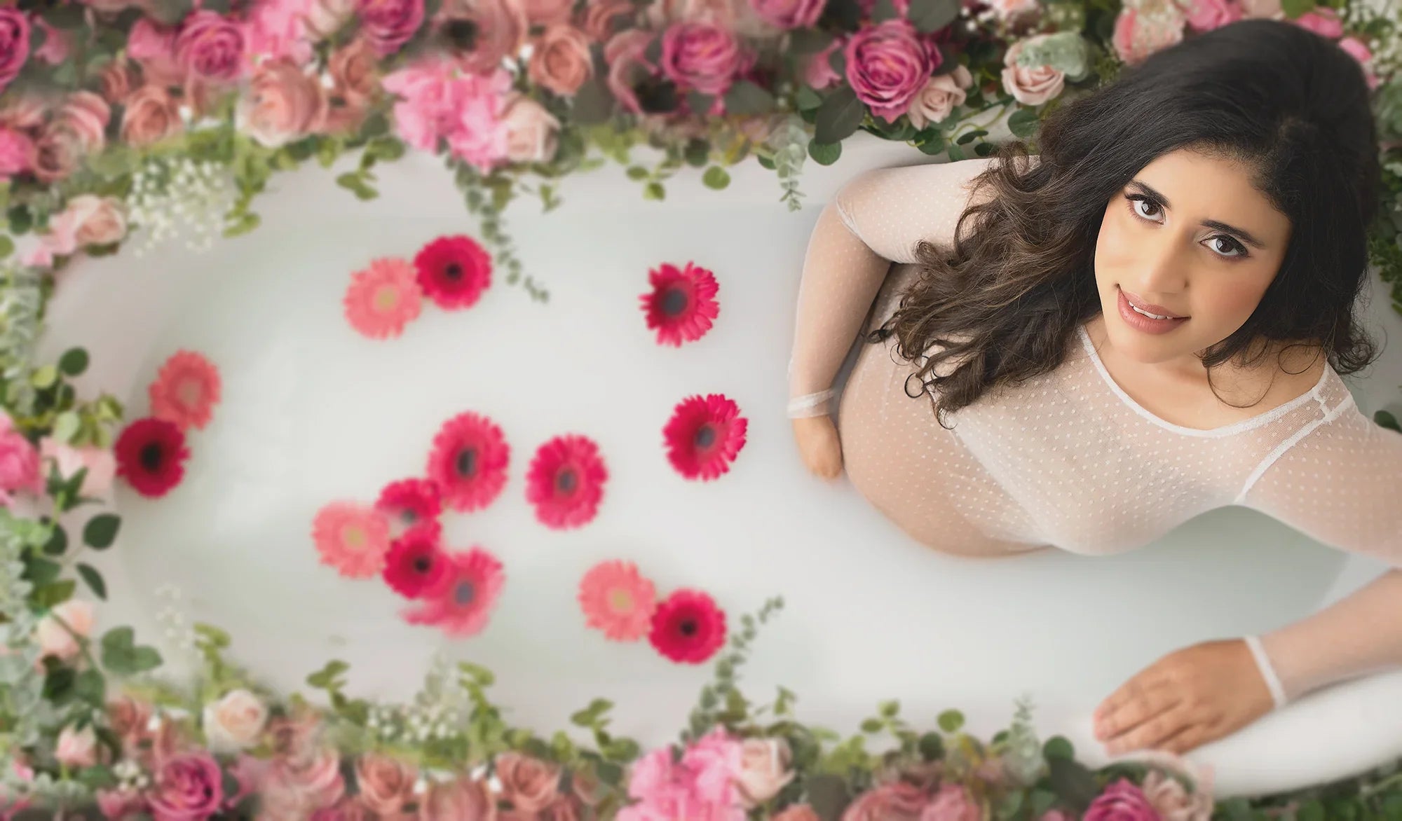 Pregnant woman in sheer polka dot maternity dress relaxing in floral milk bath