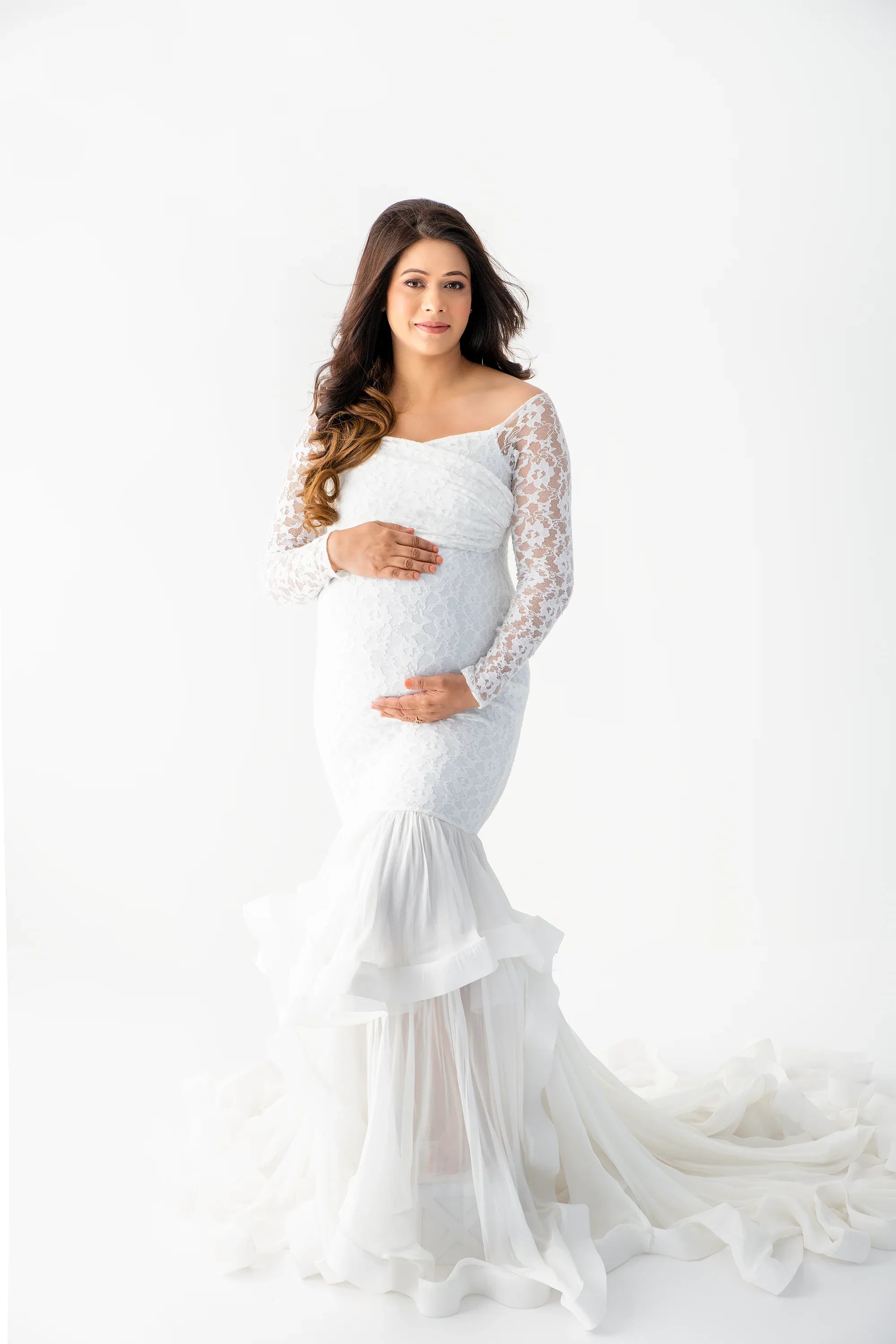 Pregnant woman wearing elegant white lace maternity gown with sheer train in studio