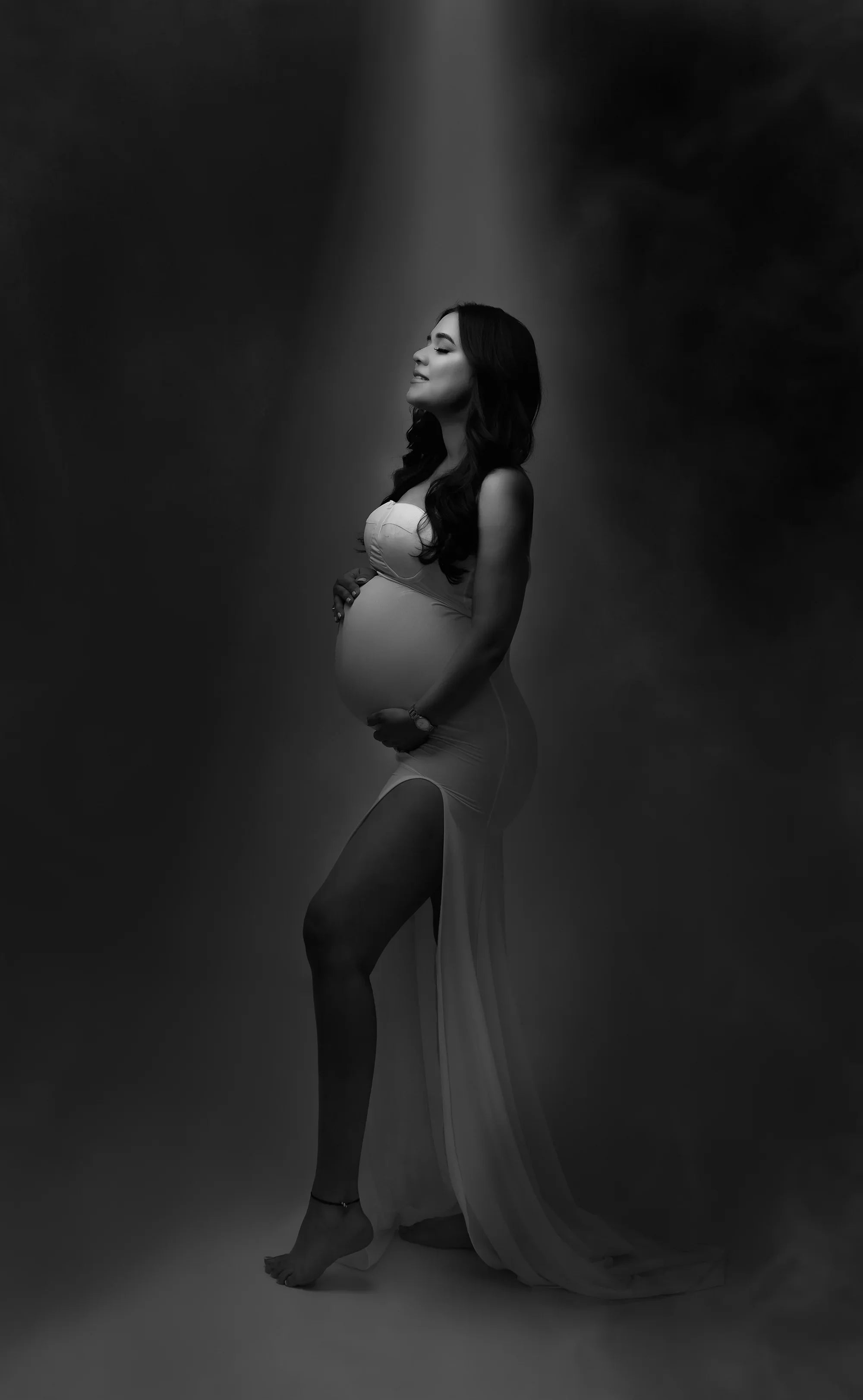 Pregnant woman in elegant maternity gown posing in studio with soft lighting