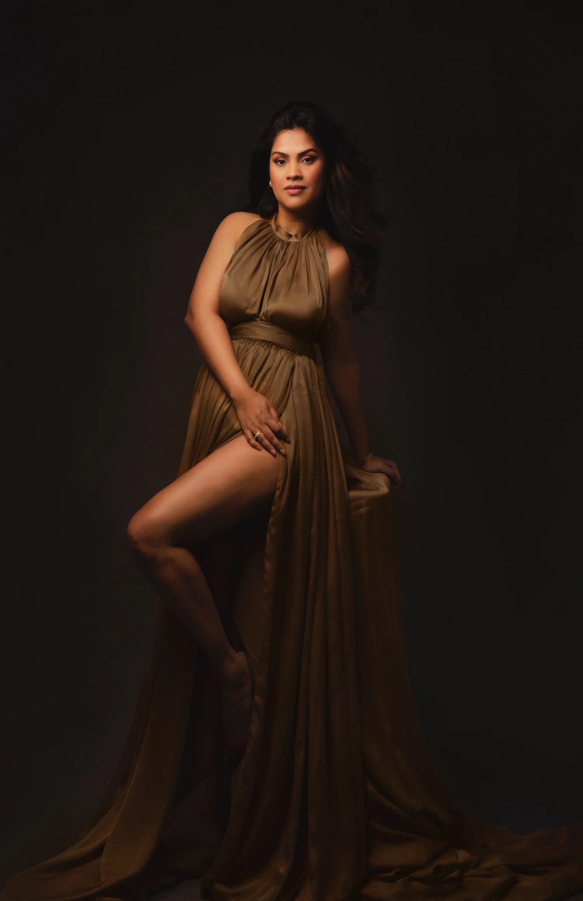 Woman in a flowing brown maternity gown with high slit, studio portrait, elegant maternity fashion