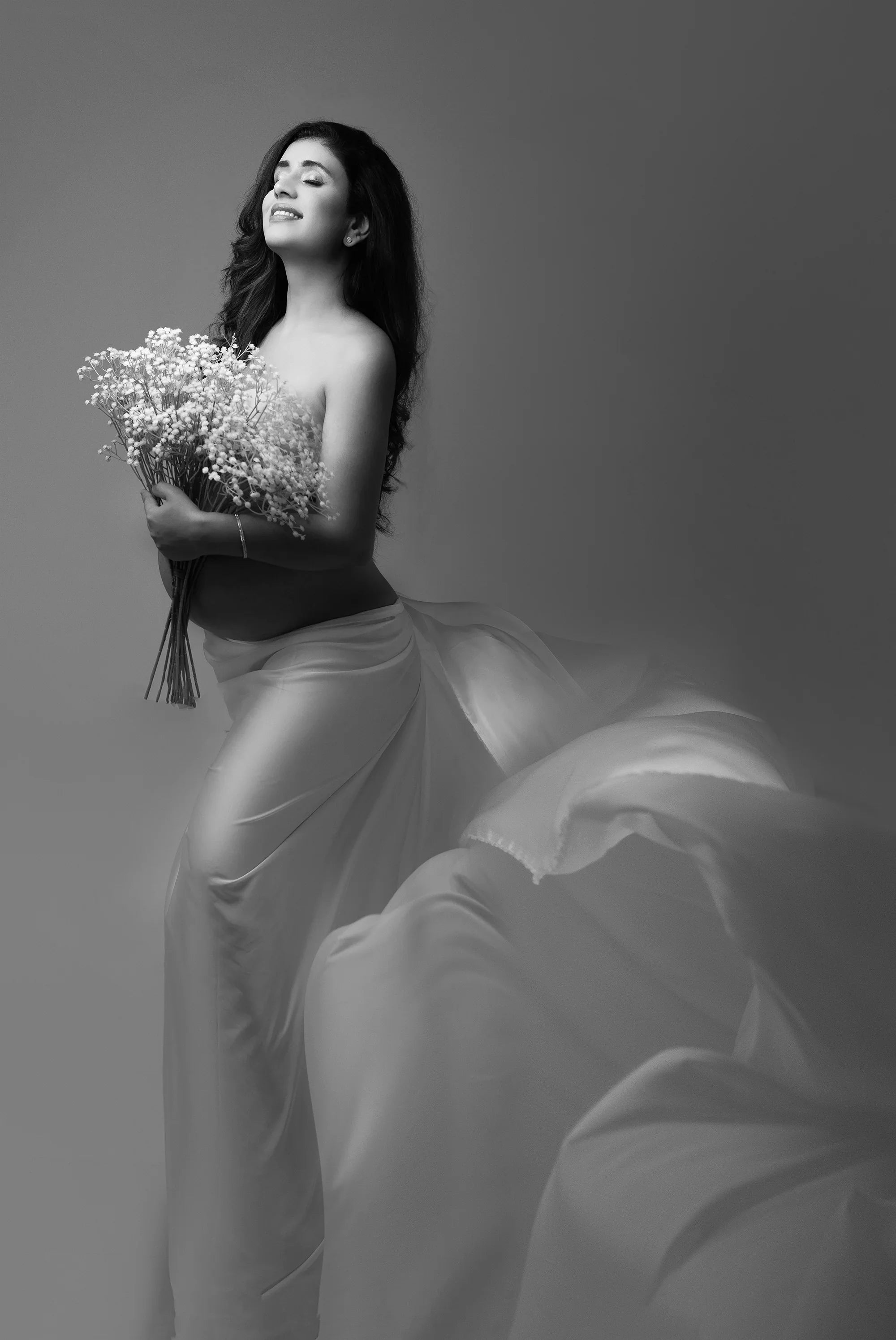 Elegant maternity photoshoot with pregnant woman in flowing gown holding flowers