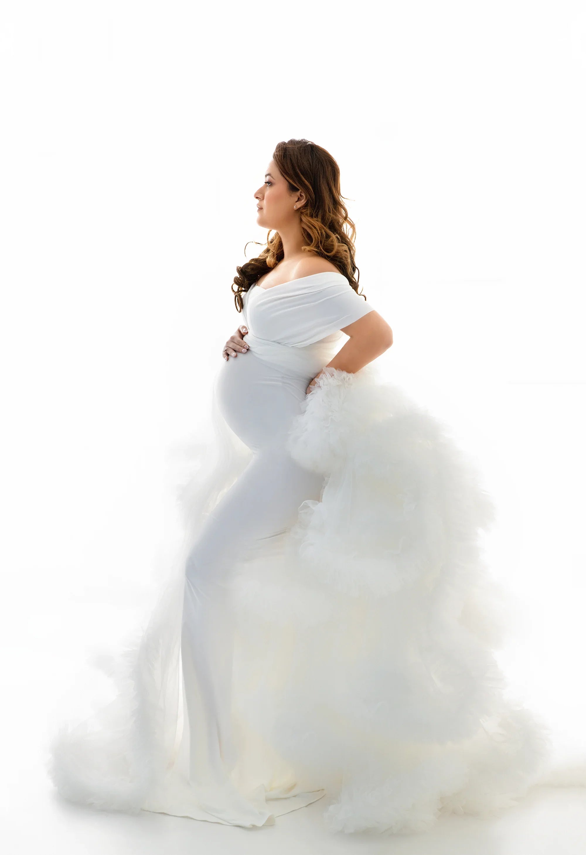 Pregnant woman in elegant white maternity gown with off-shoulder design and tulle train