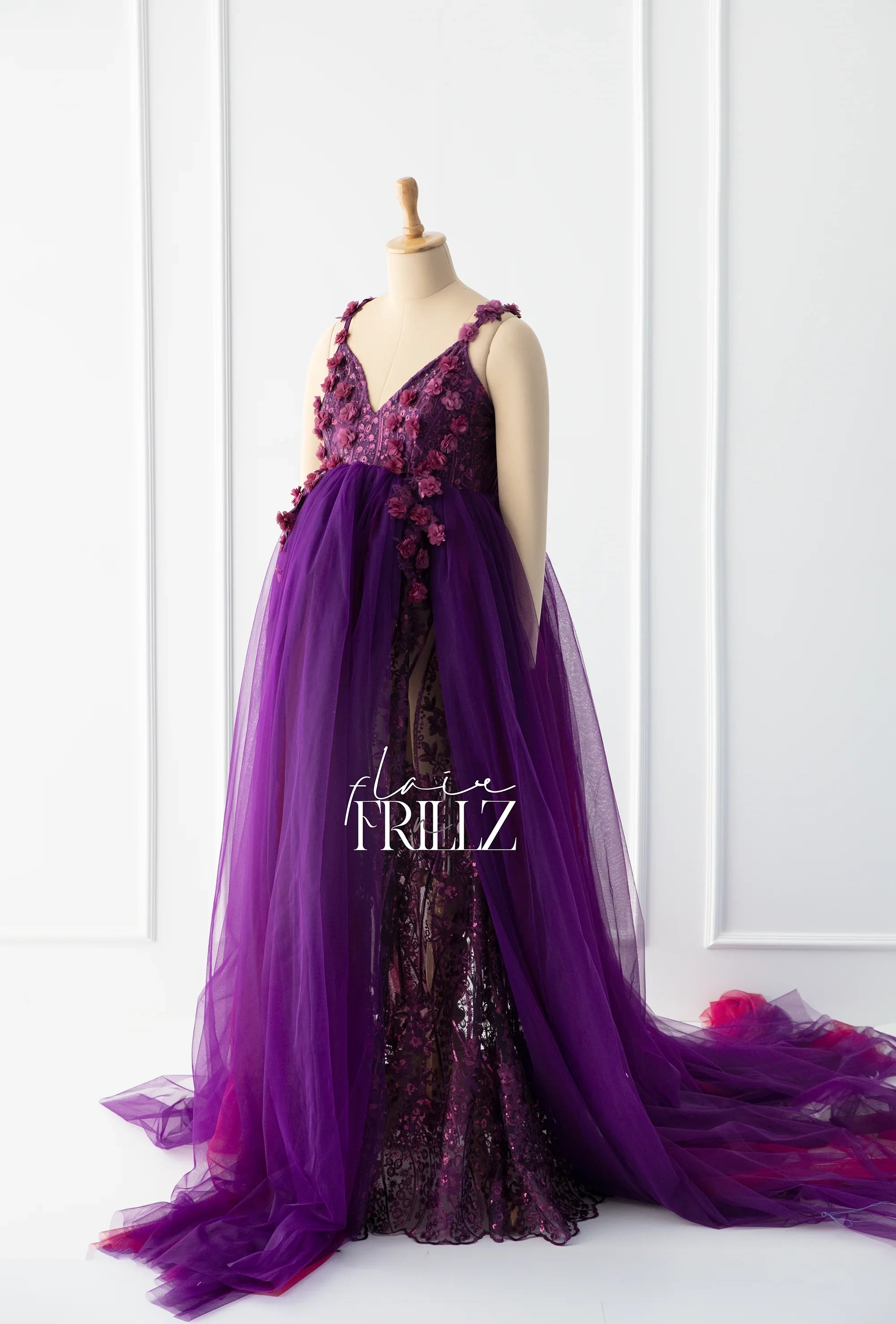 Elegant purple maternity gown with floral applique and tulle overlay on a mannequin