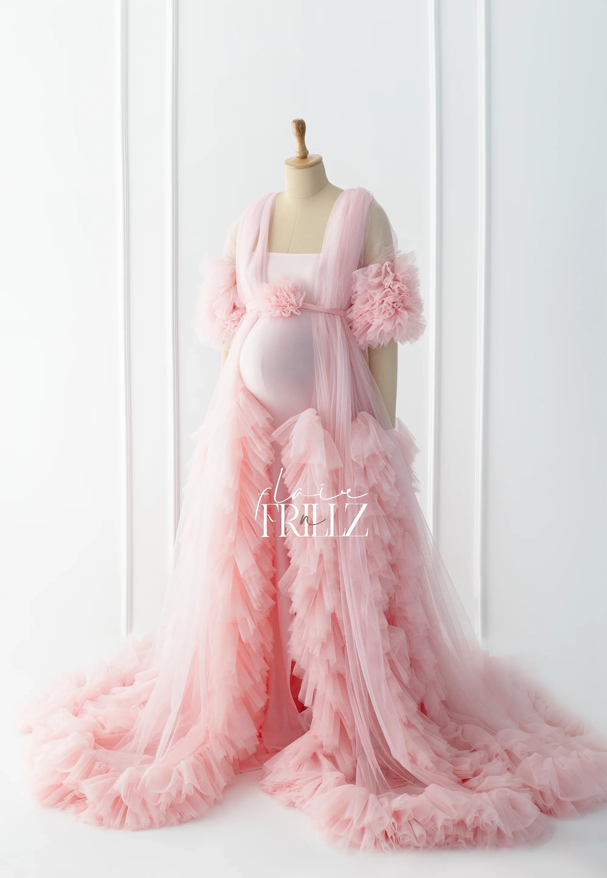 Elegant pink maternity gown with layered tulle ruffles and floral accents on mannequin