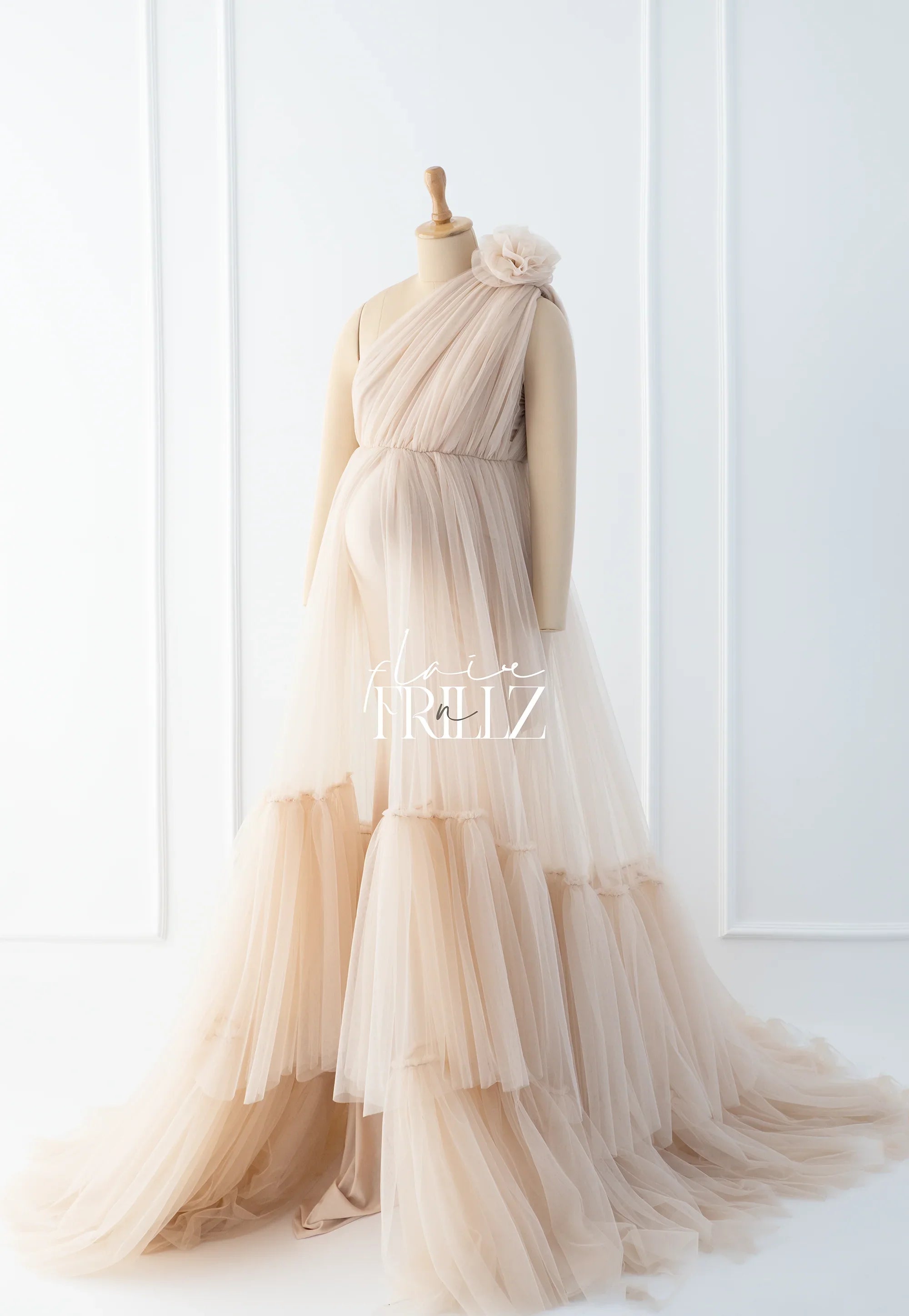 Elegant beige tulle maternity gown with one-shoulder design and tiered skirt on mannequin