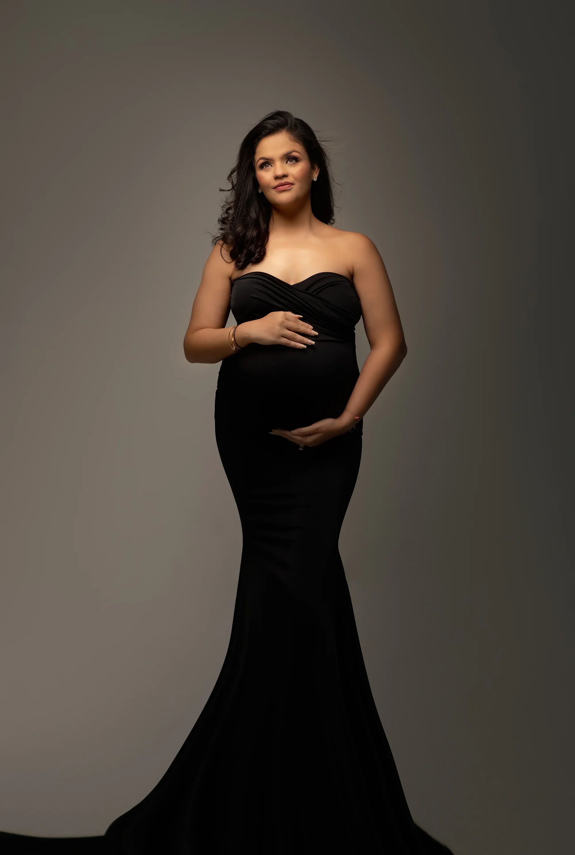 Elegant pregnant woman in strapless black maternity gown against neutral background