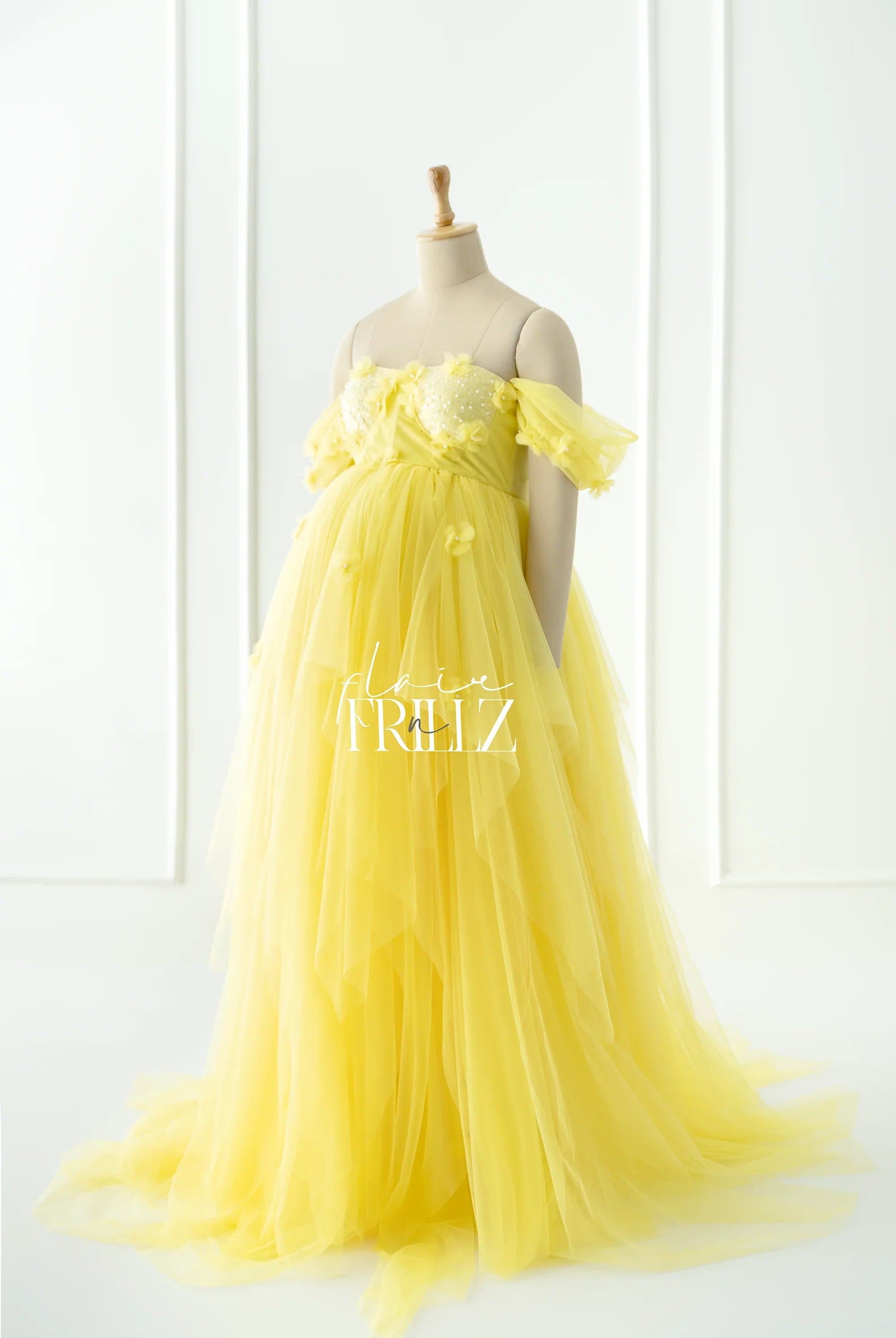 Yellow maternity gown with off-shoulder sleeves and floral appliques on mannequin