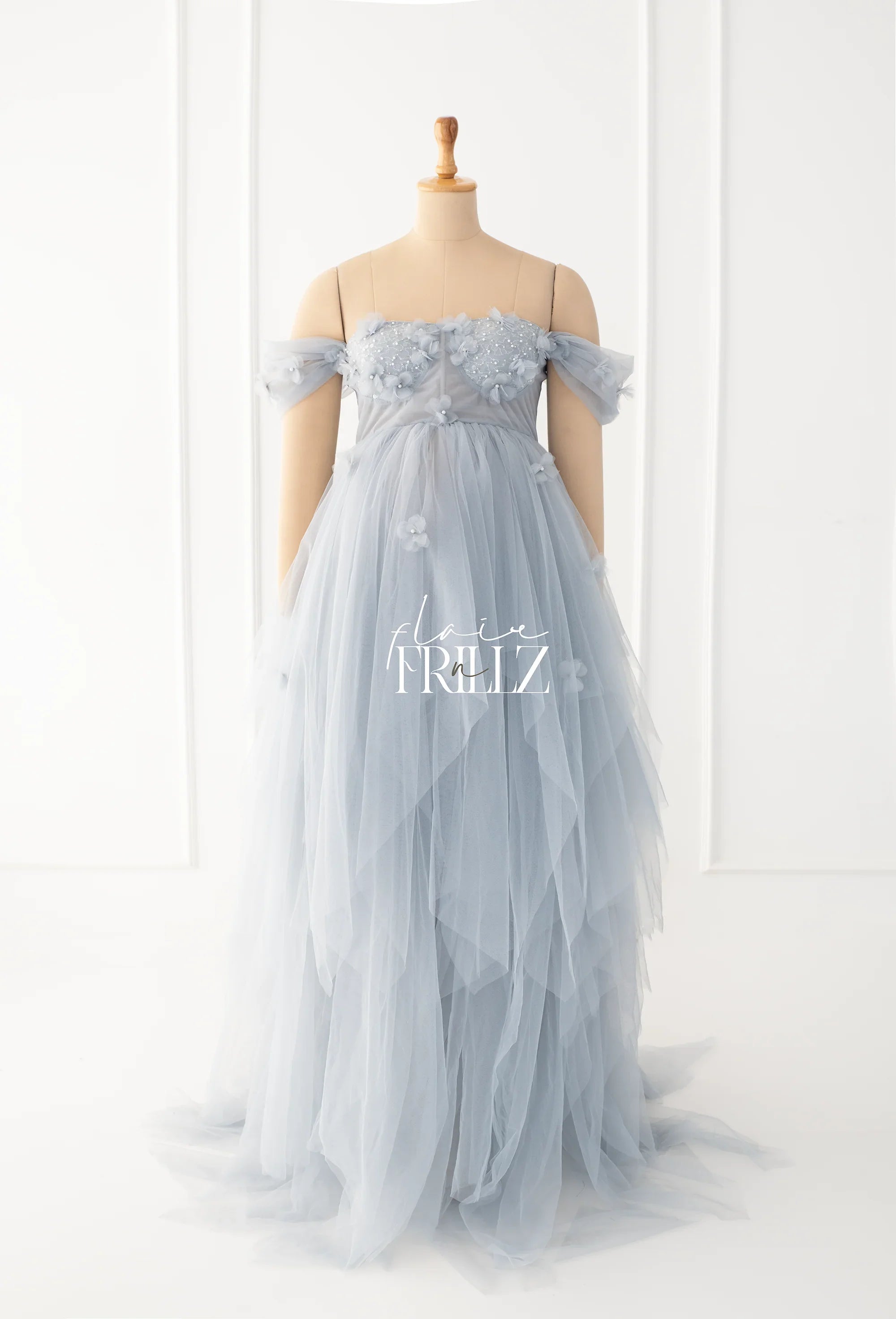 Light blue off-shoulder tulle maternity gown with floral appliqués on a mannequin