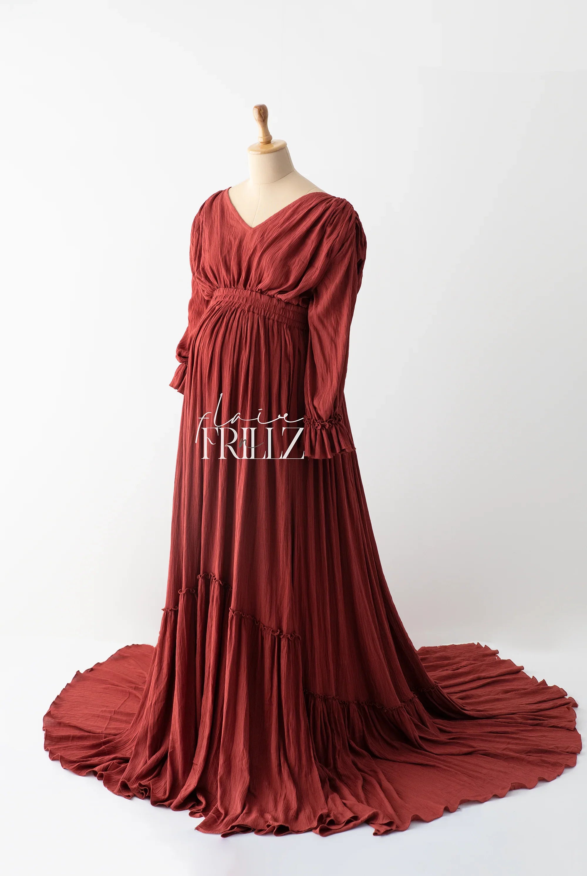 Rust red maternity gown with long sleeves and flowing train on mannequin