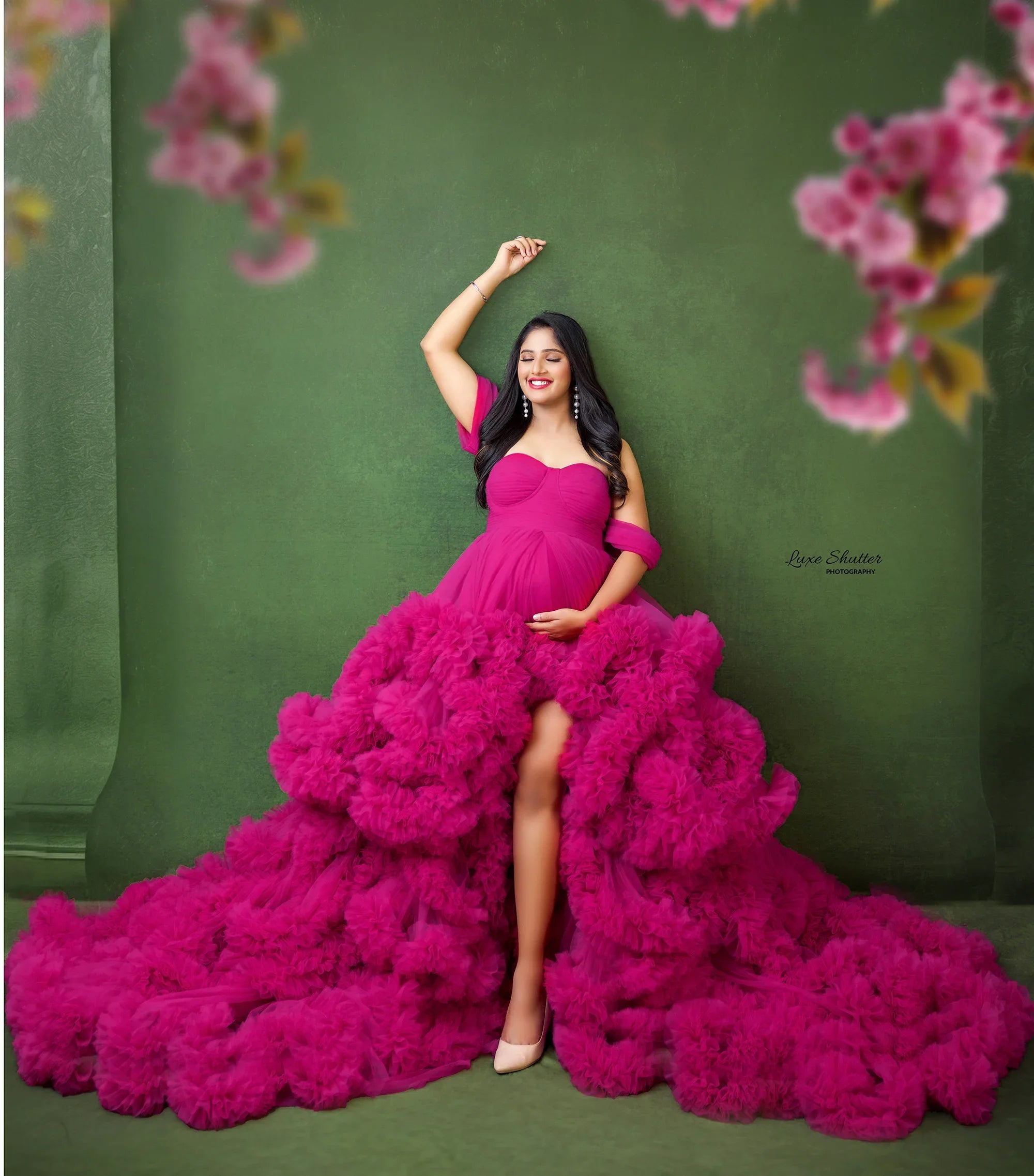 Pregnant woman in vibrant magenta ruffled maternity gown posing against a green backdrop