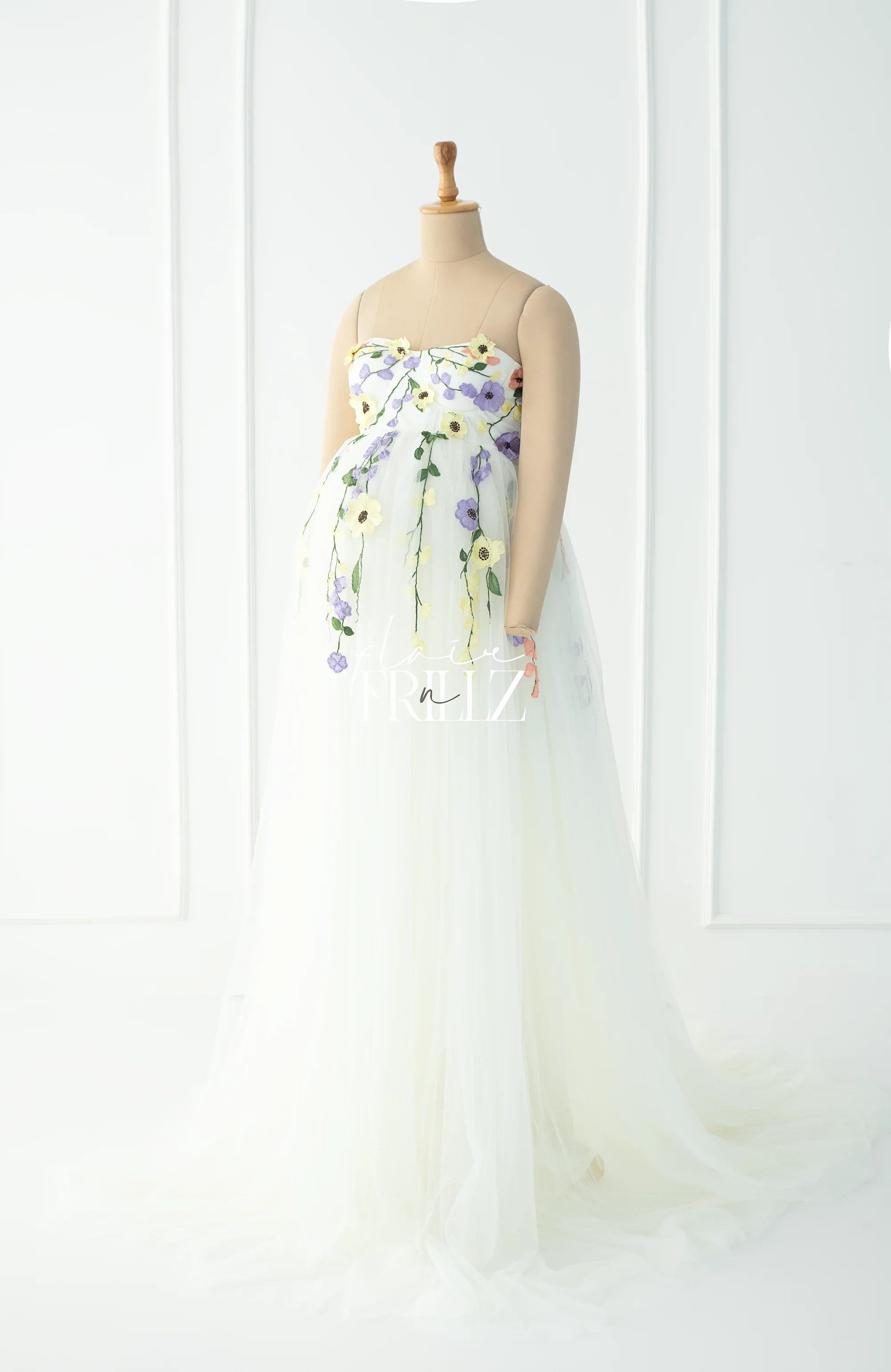 Sleeveless white maternity gown with yellow and purple floral embroidery on a mannequin