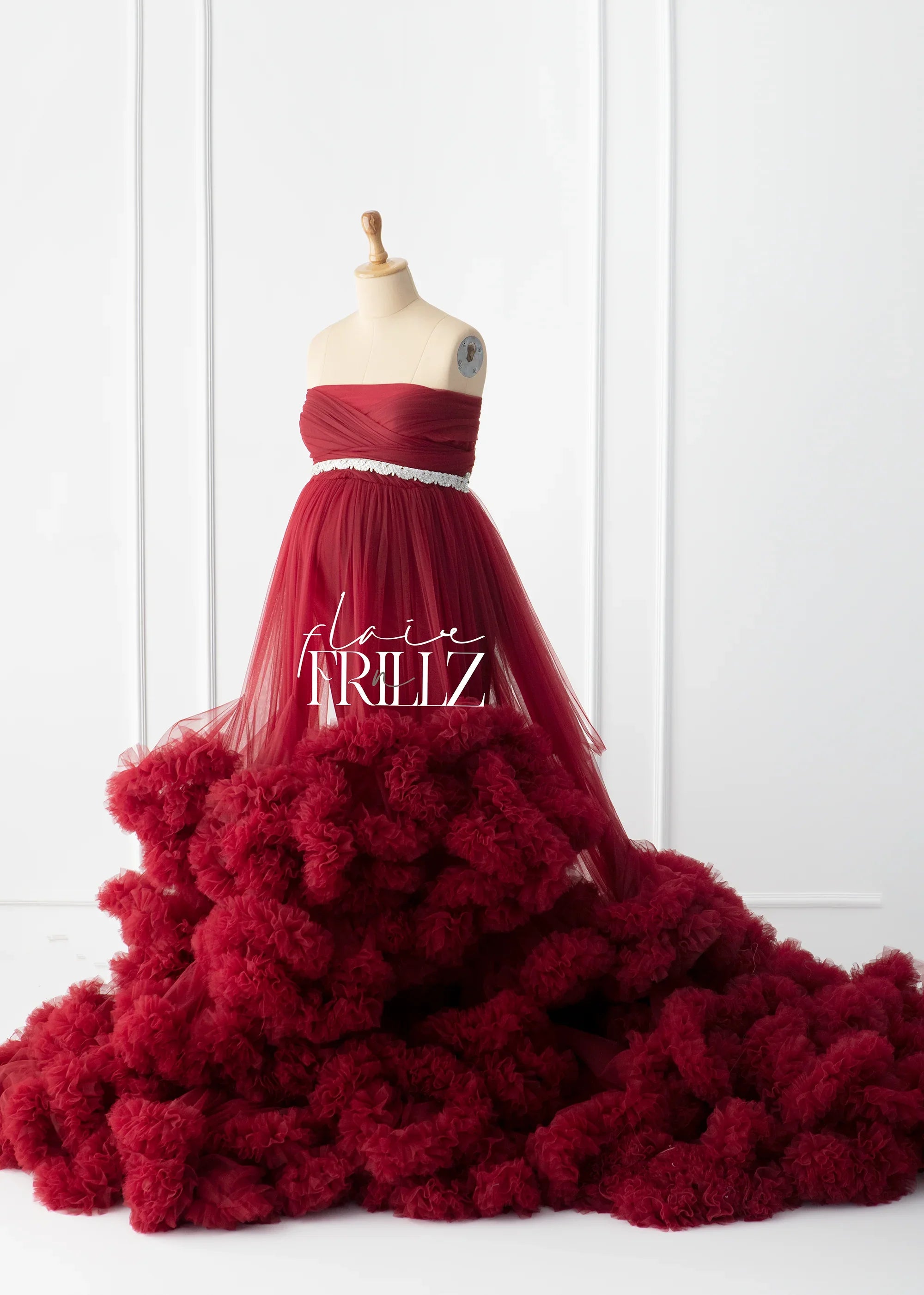 Burgundy strapless maternity gown with tulle skirt and ruffled train on dress form