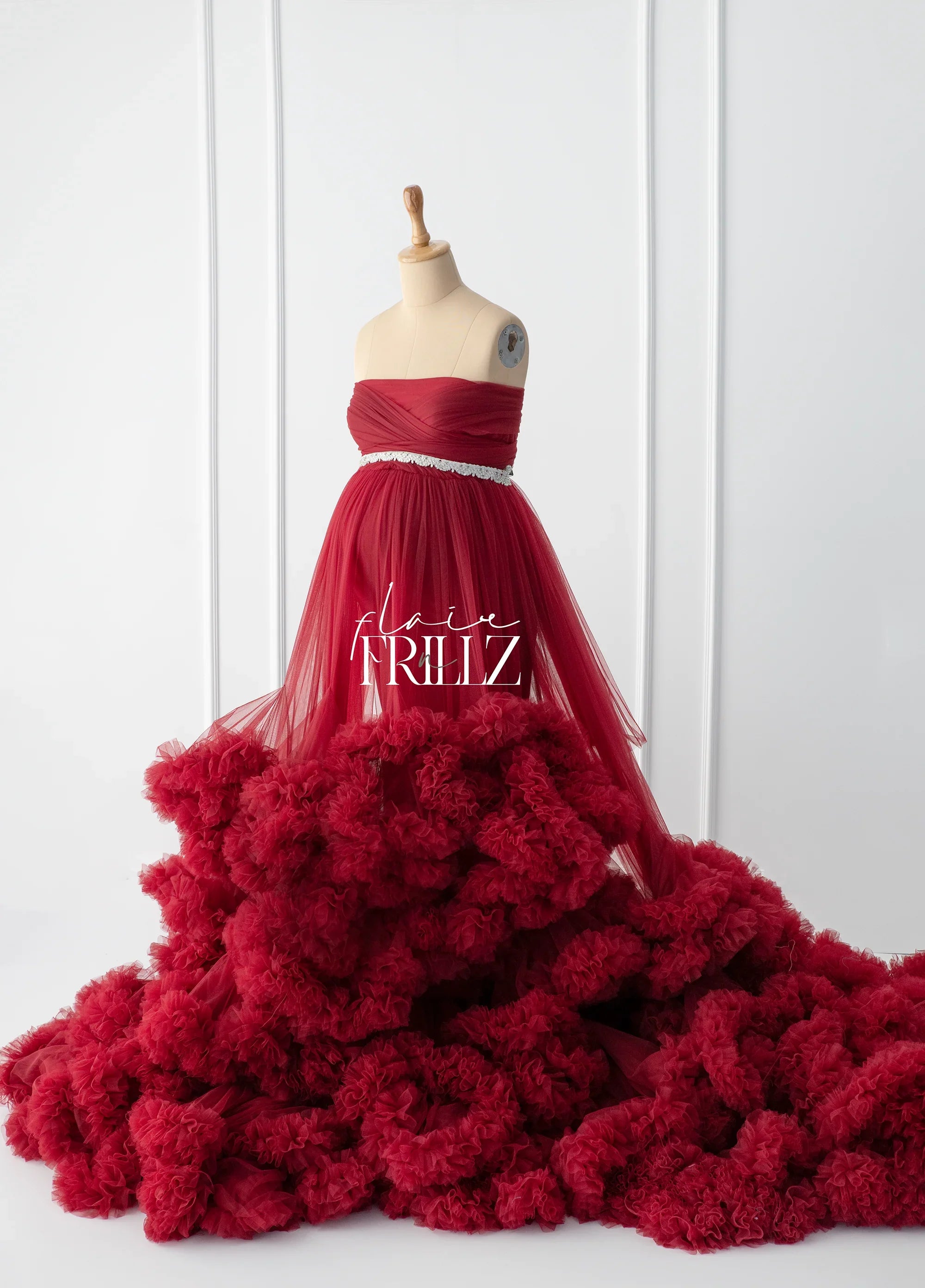 Elegant red maternity gown with tulle layers and ruffled skirt on dress form