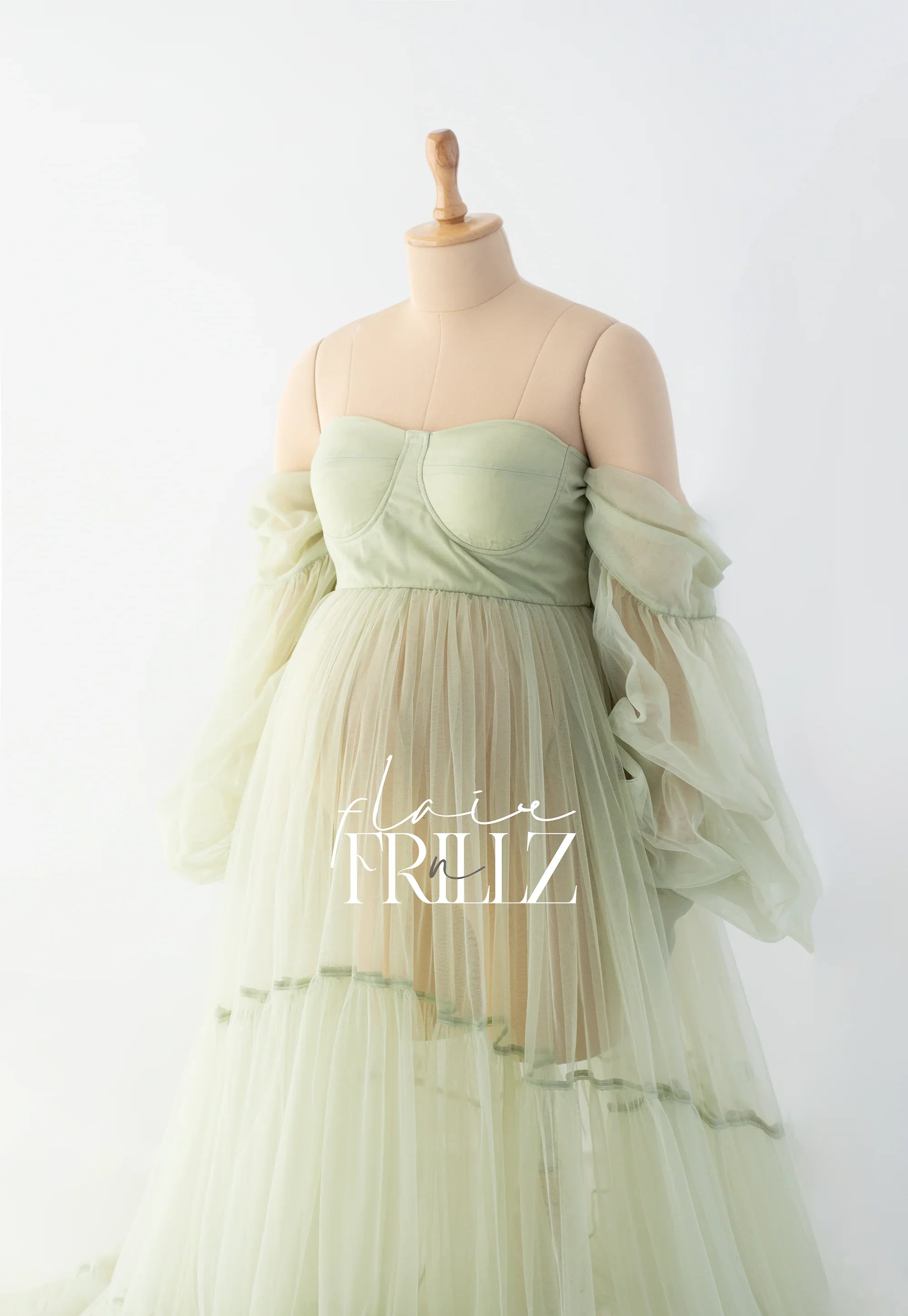 Light green off-shoulder maternity gown with sheer tulle sleeves on a mannequin