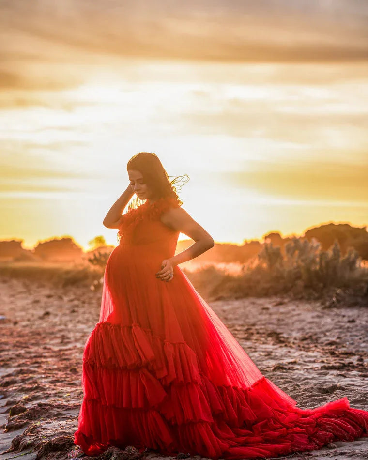 Pregnant woman in a flowing red maternity gown posing outdoors at sunset