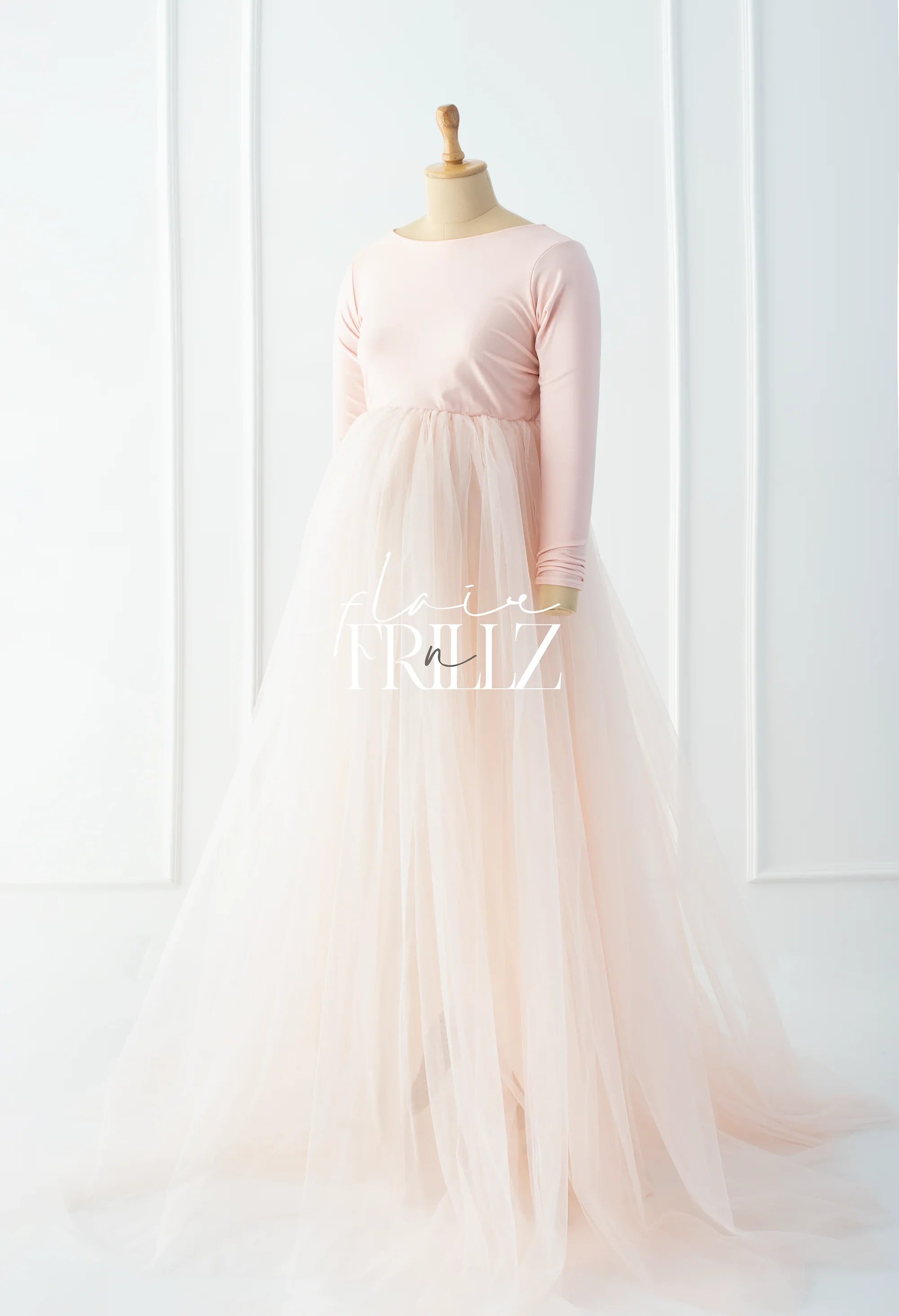Peach maternity gown with long sleeves and tulle skirt on mannequin in bright studio