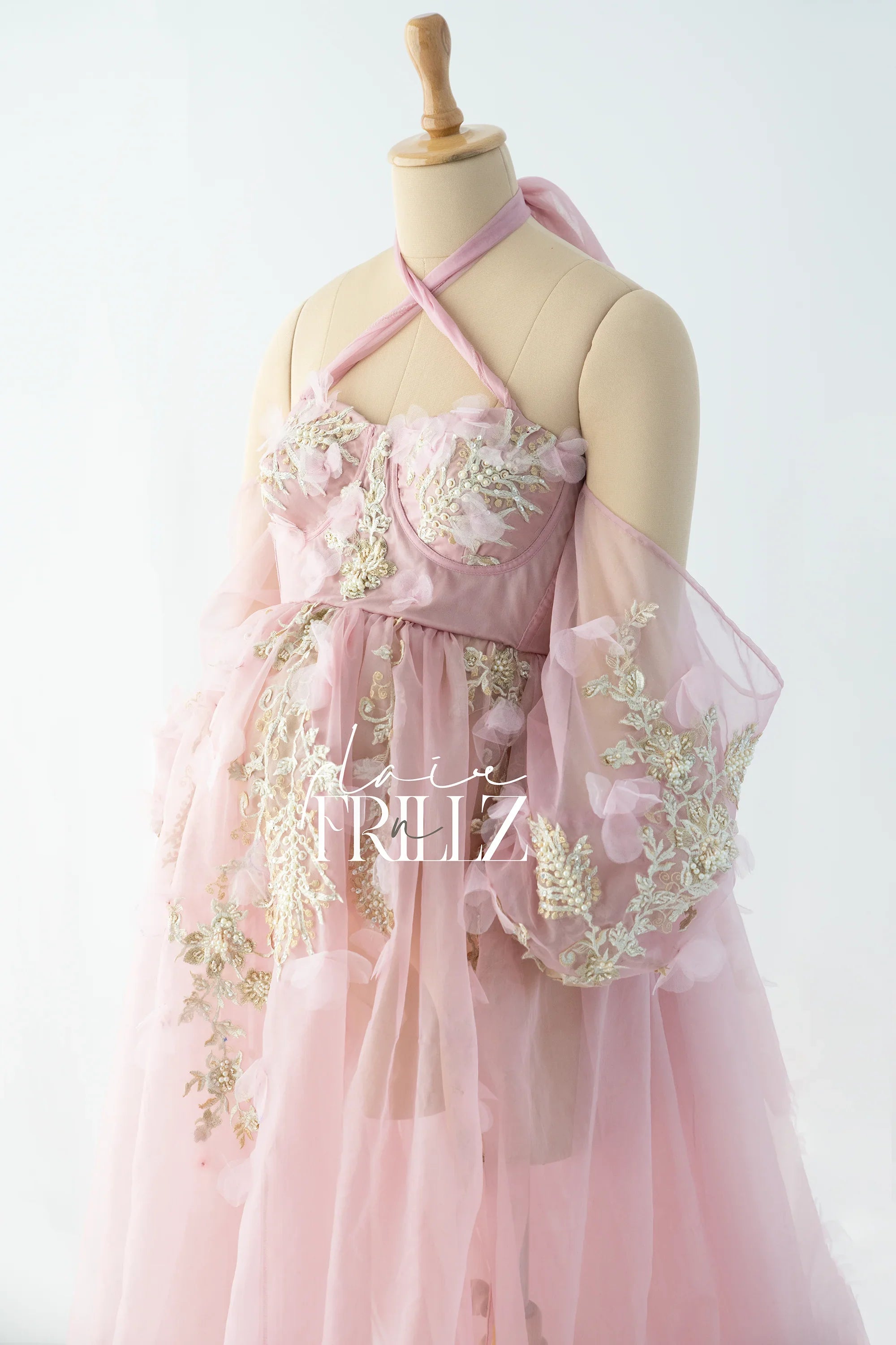 Pink maternity gown with sheer off-shoulder sleeves and floral embroidery on a mannequin