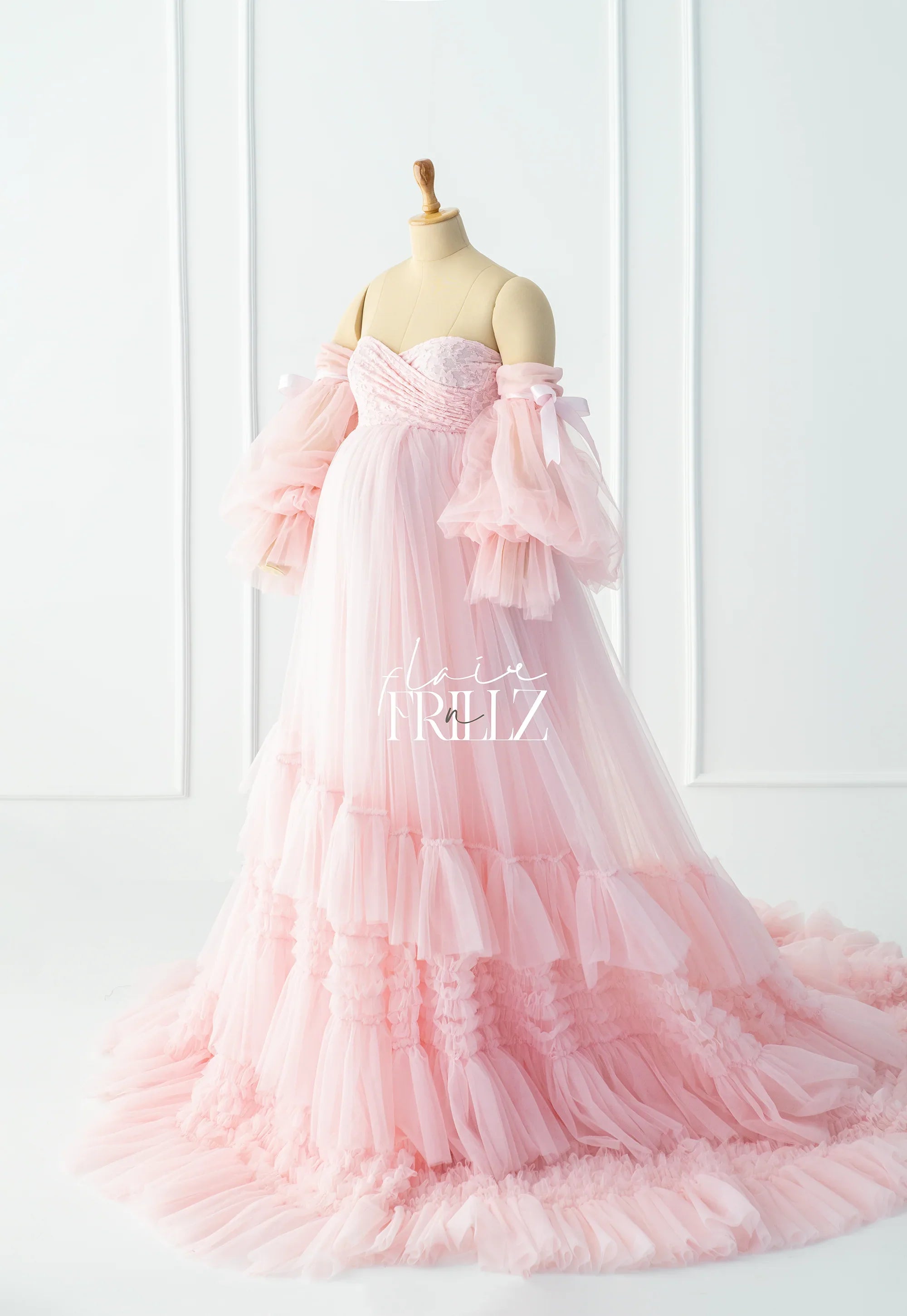 Pink maternity gown with ruffled tulle layers and off-shoulder sleeves on a mannequin
