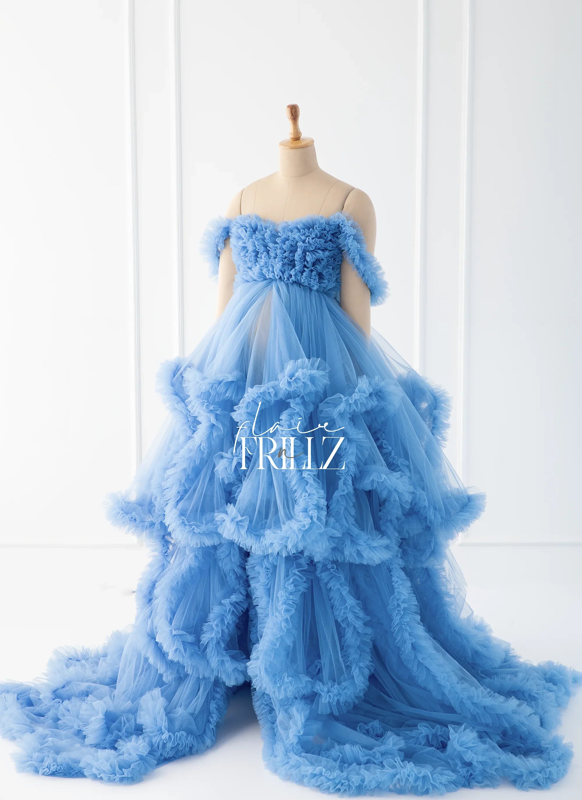 Elegant blue tulle maternity gown with ruffled layers on a mannequin in a bright room