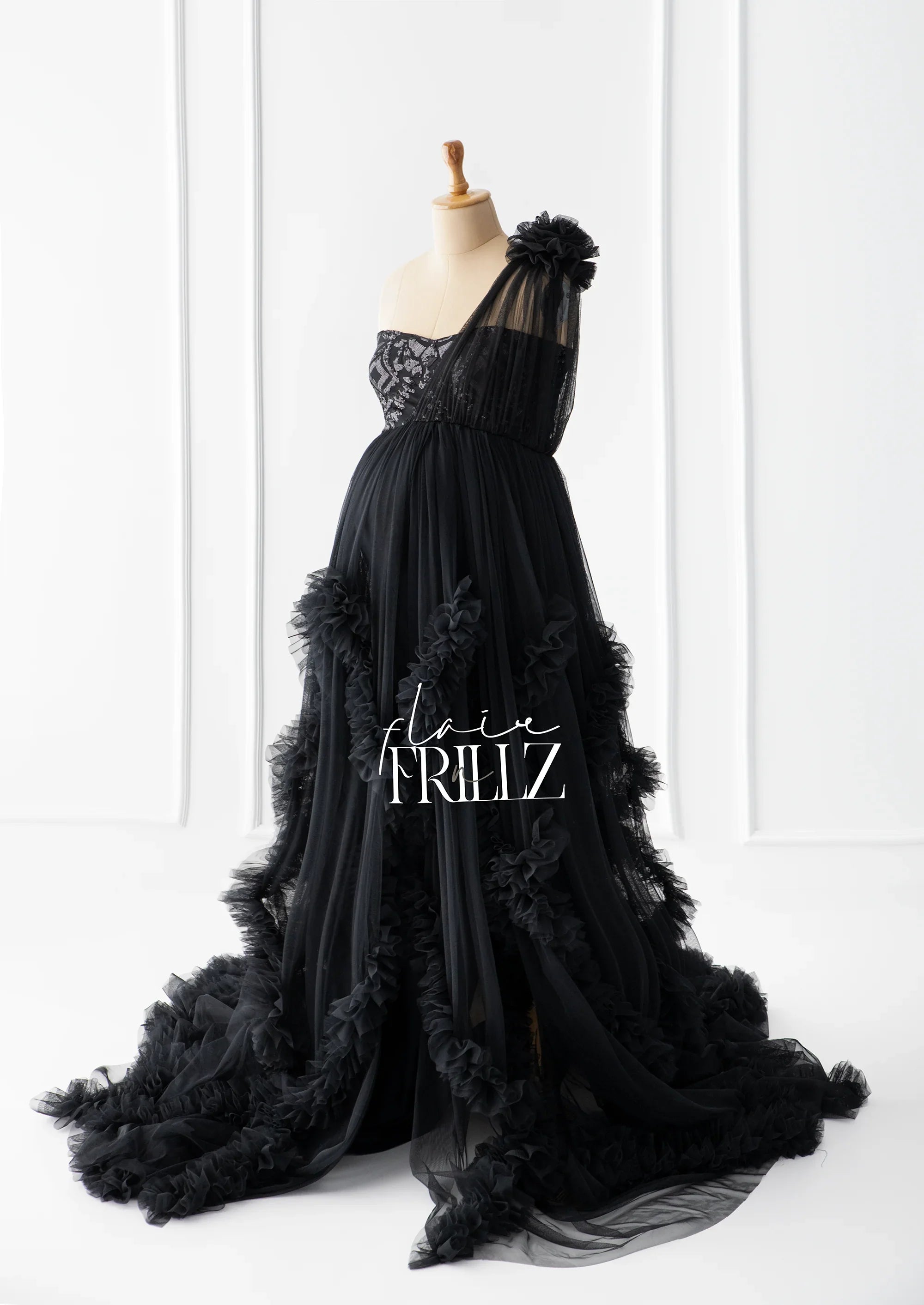 Elegant black maternity gown with tulle layers, floral accents, and one-shoulder design on mannequin.