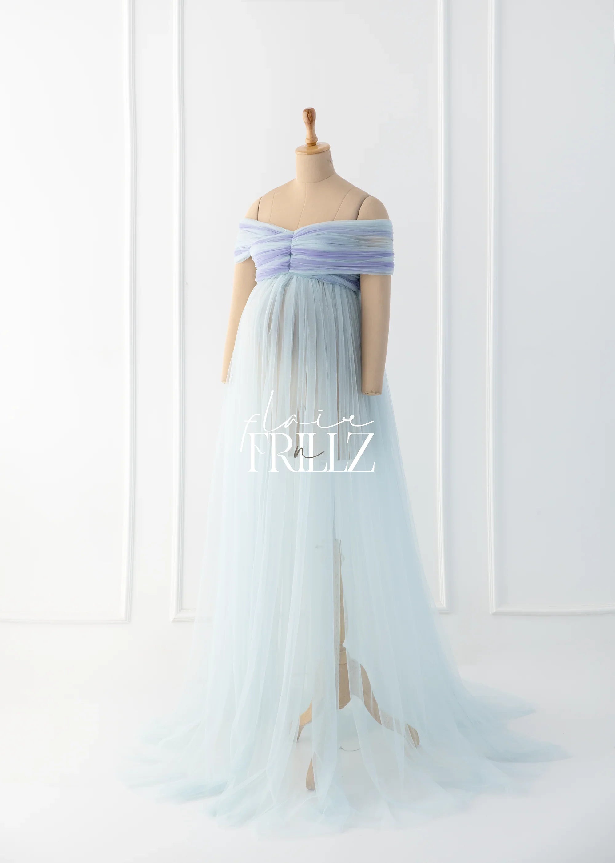 Light blue off-shoulder maternity gown with tulle overlay on a mannequin in a bright studio