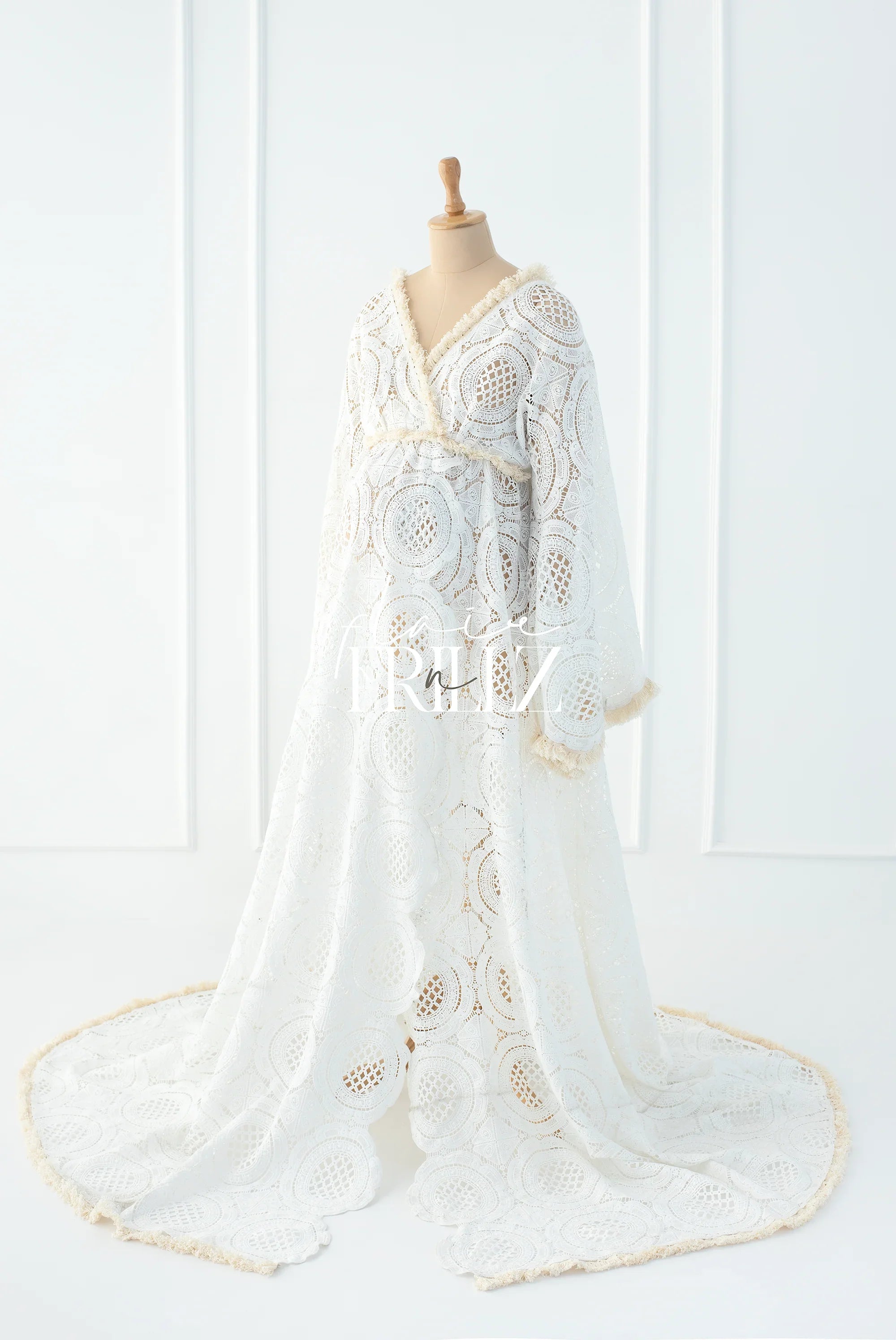 White boho maternity gown with lace pattern and fringe details on mannequin in studio setting