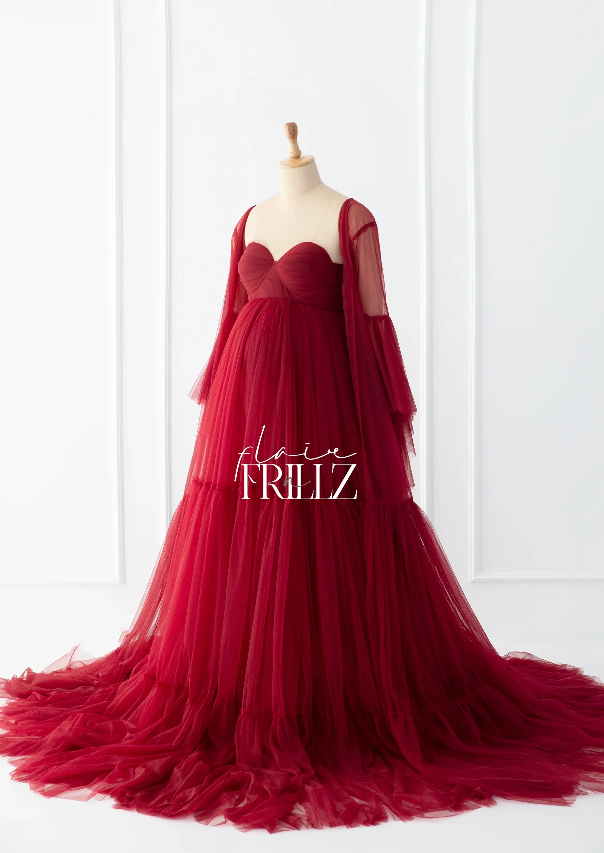 Elegant burgundy maternity gown with tulle layers and sheer long sleeves on a mannequin