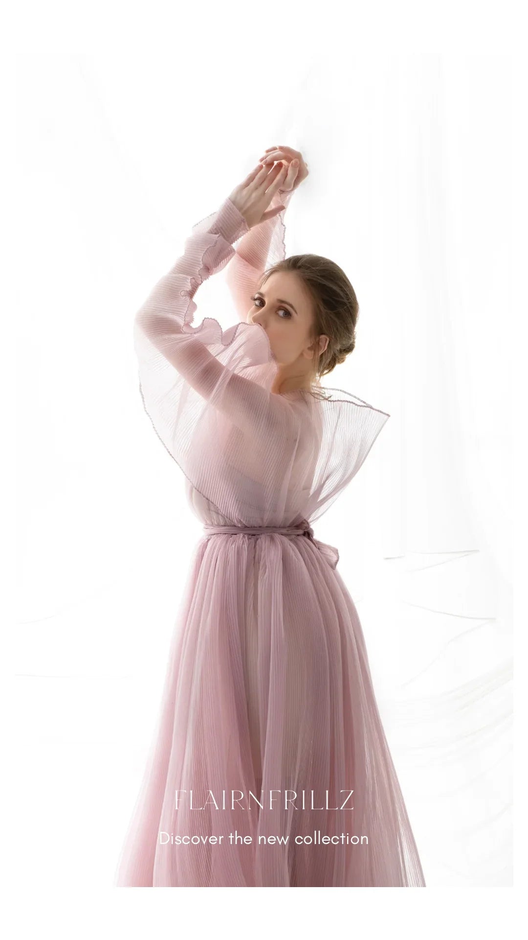 Woman in sheer pink maternity gown with ruffled sleeves, posing gracefully in soft light