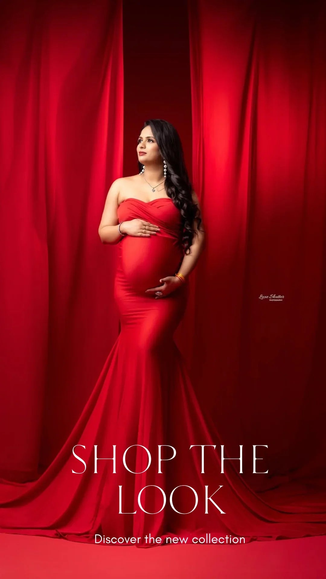 Elegant pregnant woman in a strapless red maternity gown posing against red curtains