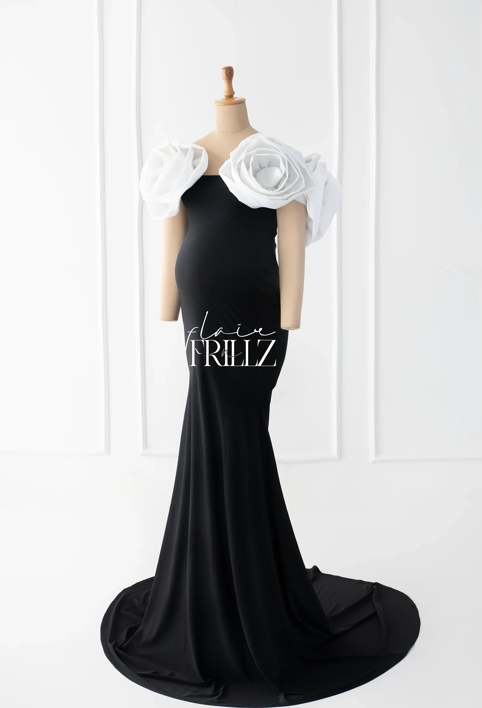 Black maternity gown with large white floral shoulder accents on mannequin, floor-length design