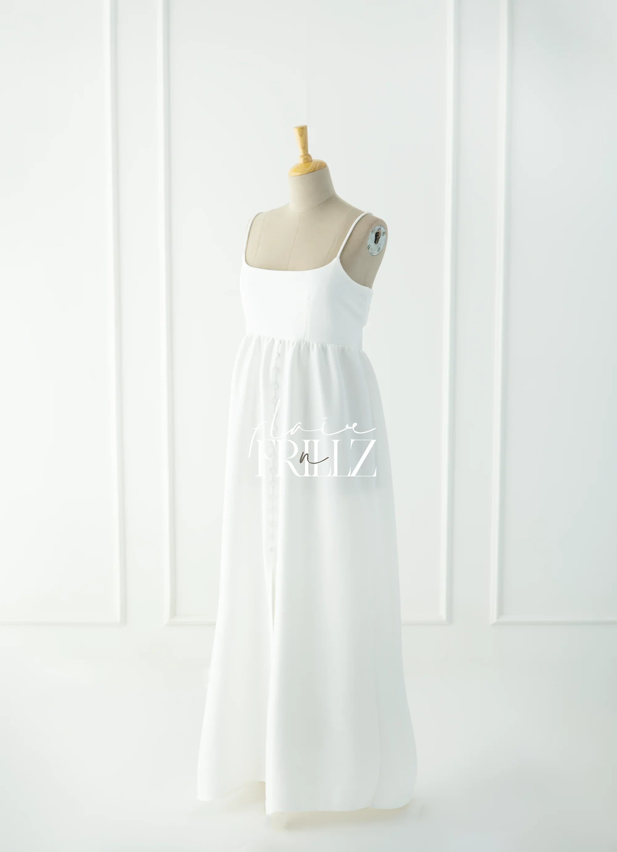 Elegant white maternity gown with spaghetti straps and button details, displayed on a mannequin.