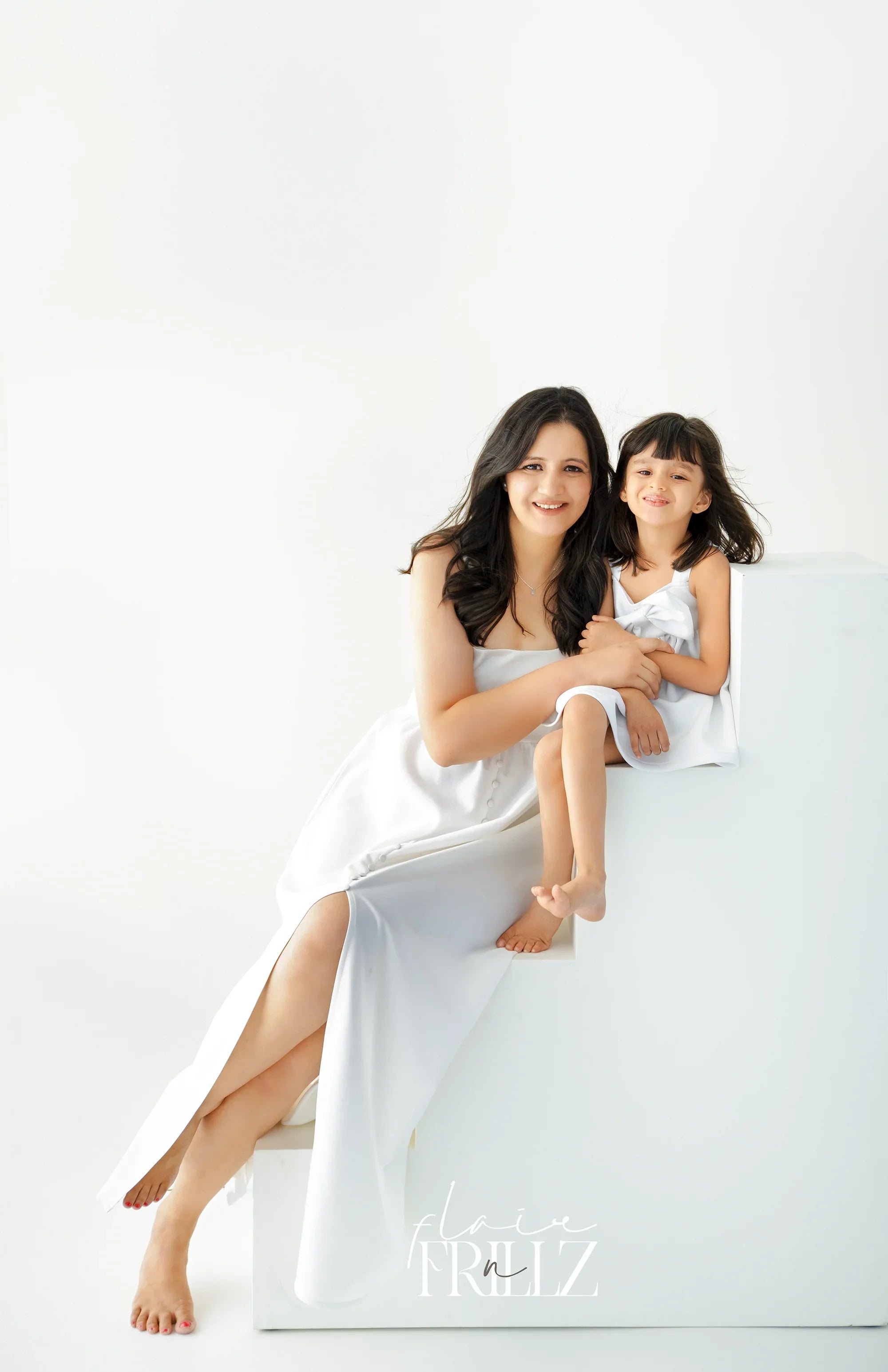 Smiling woman and little girl in matching white dresses, posing in a bright studio