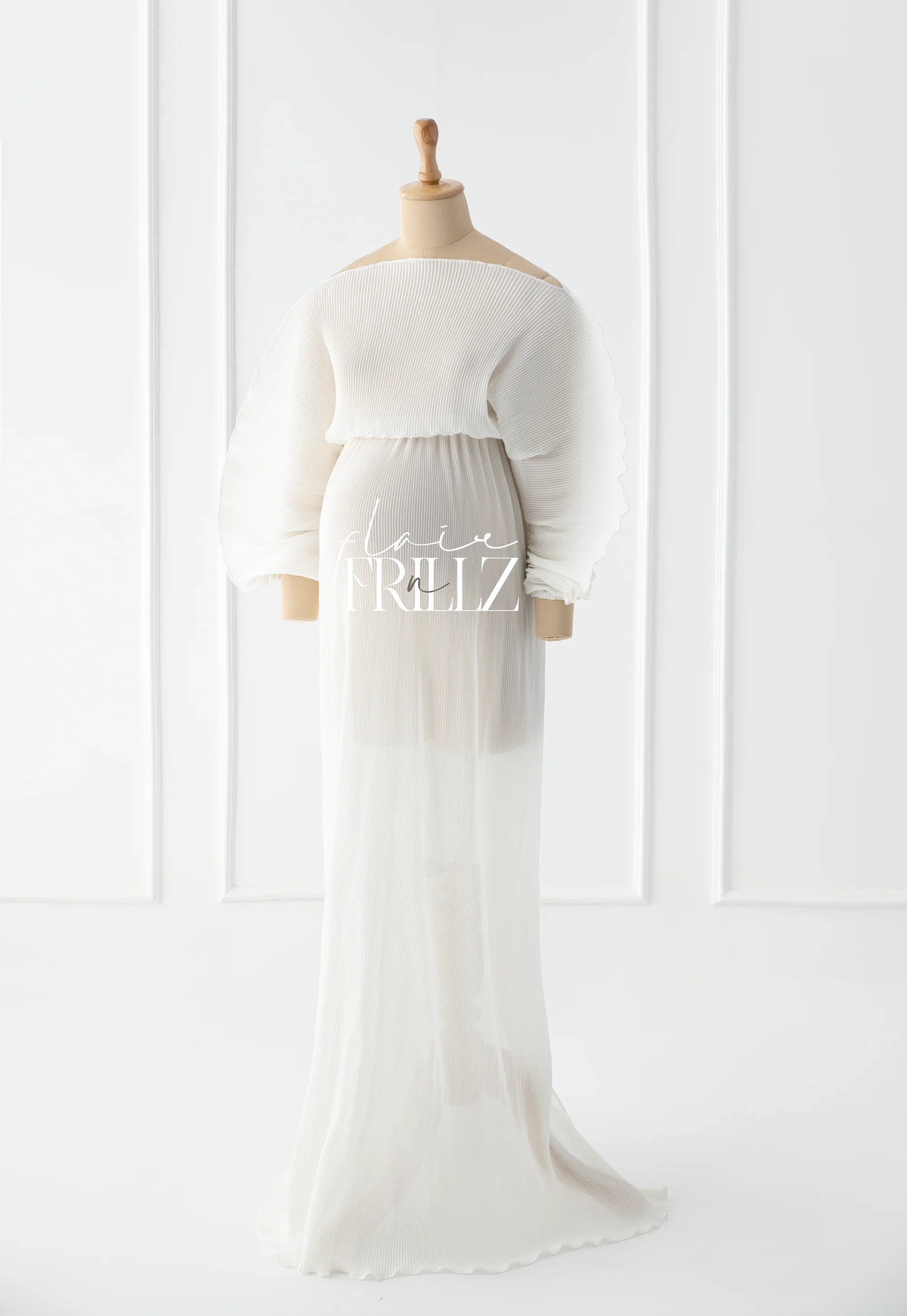 Elegant pleated maternity gown with sheer long sleeves on a mannequin in a bright studio