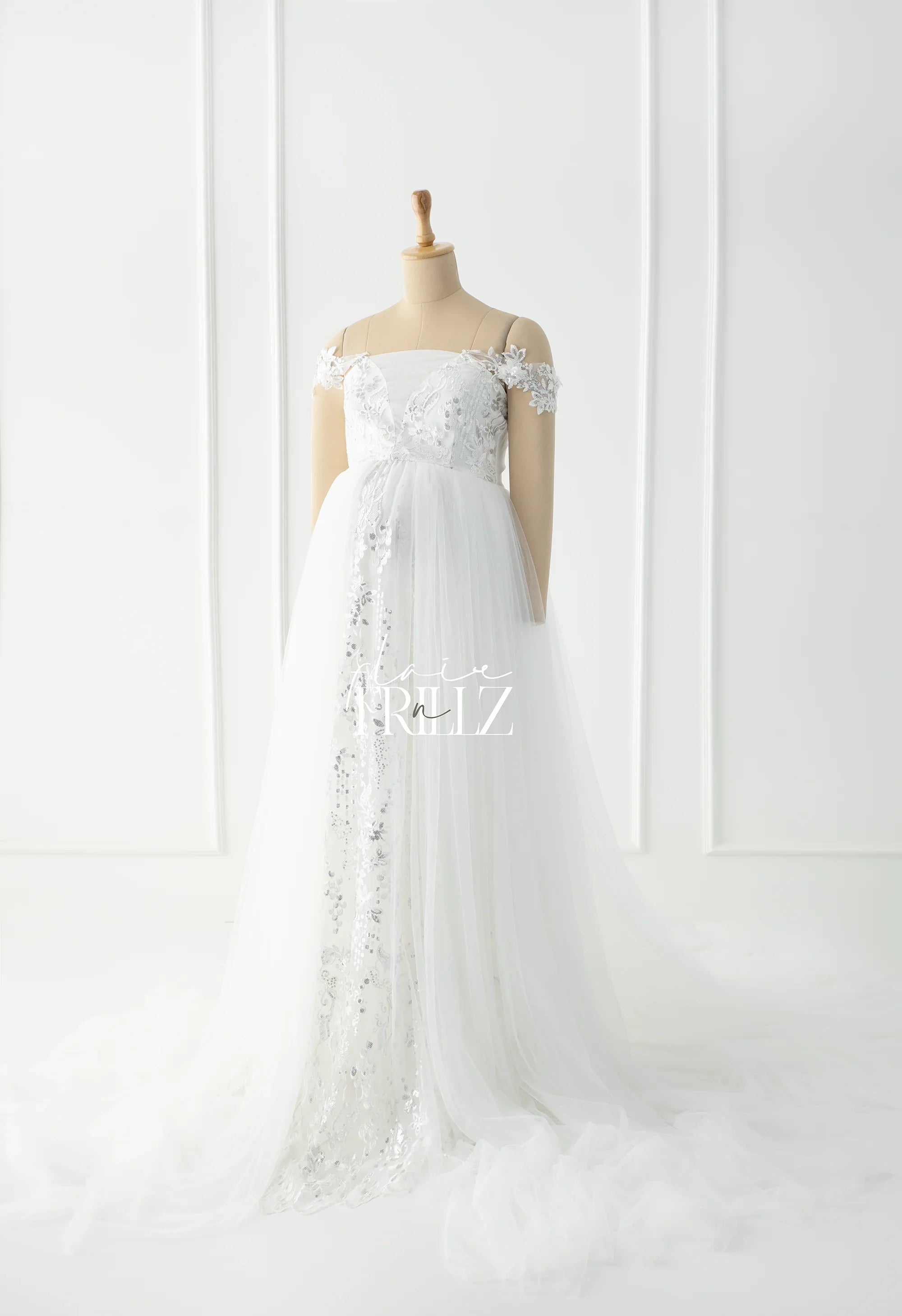 White sequin off-shoulder maternity gown with floral lace on mannequin in a bright studio