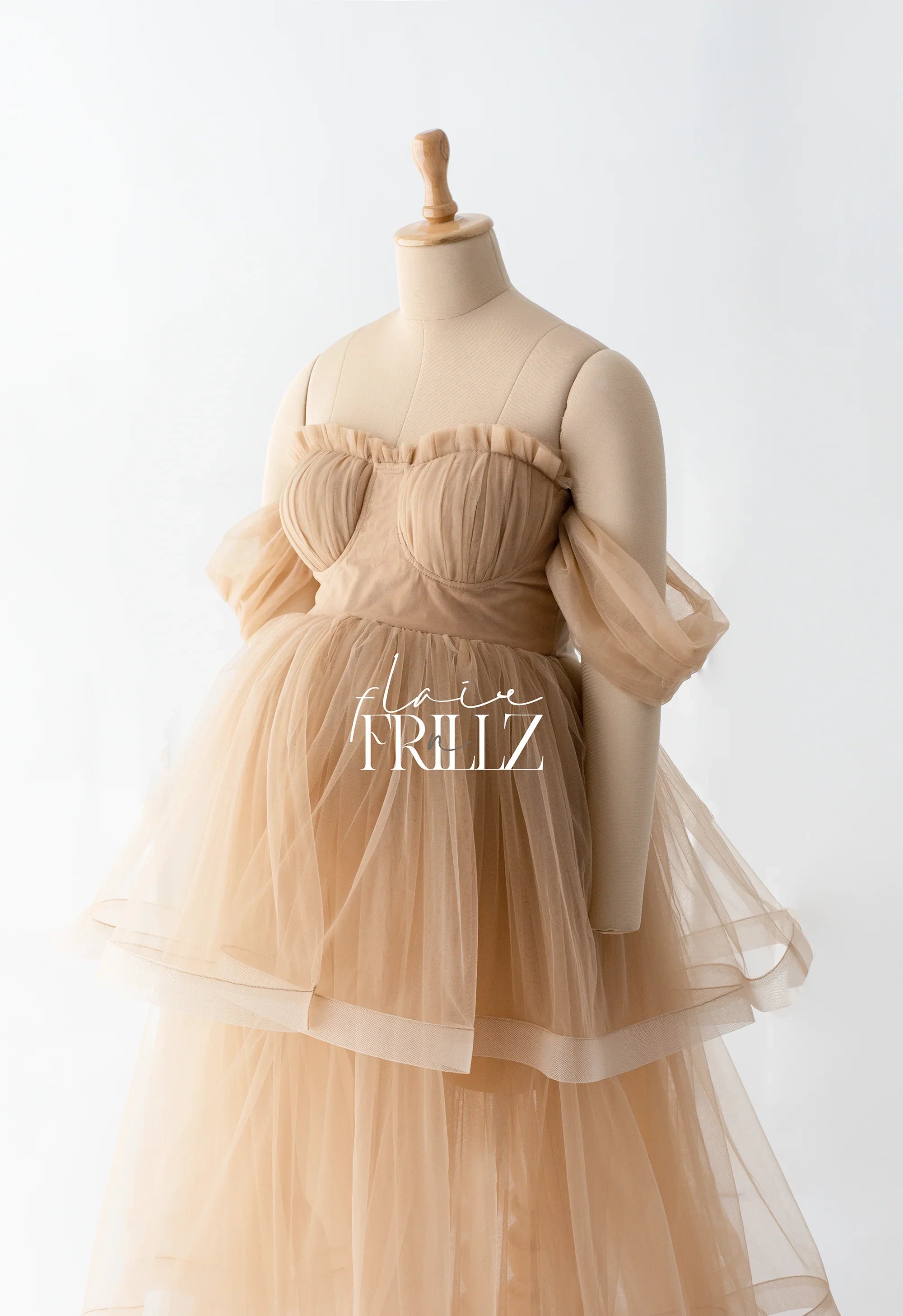 Beige tulle maternity gown with off-shoulder sleeves on a dress form, ideal for photoshoots.