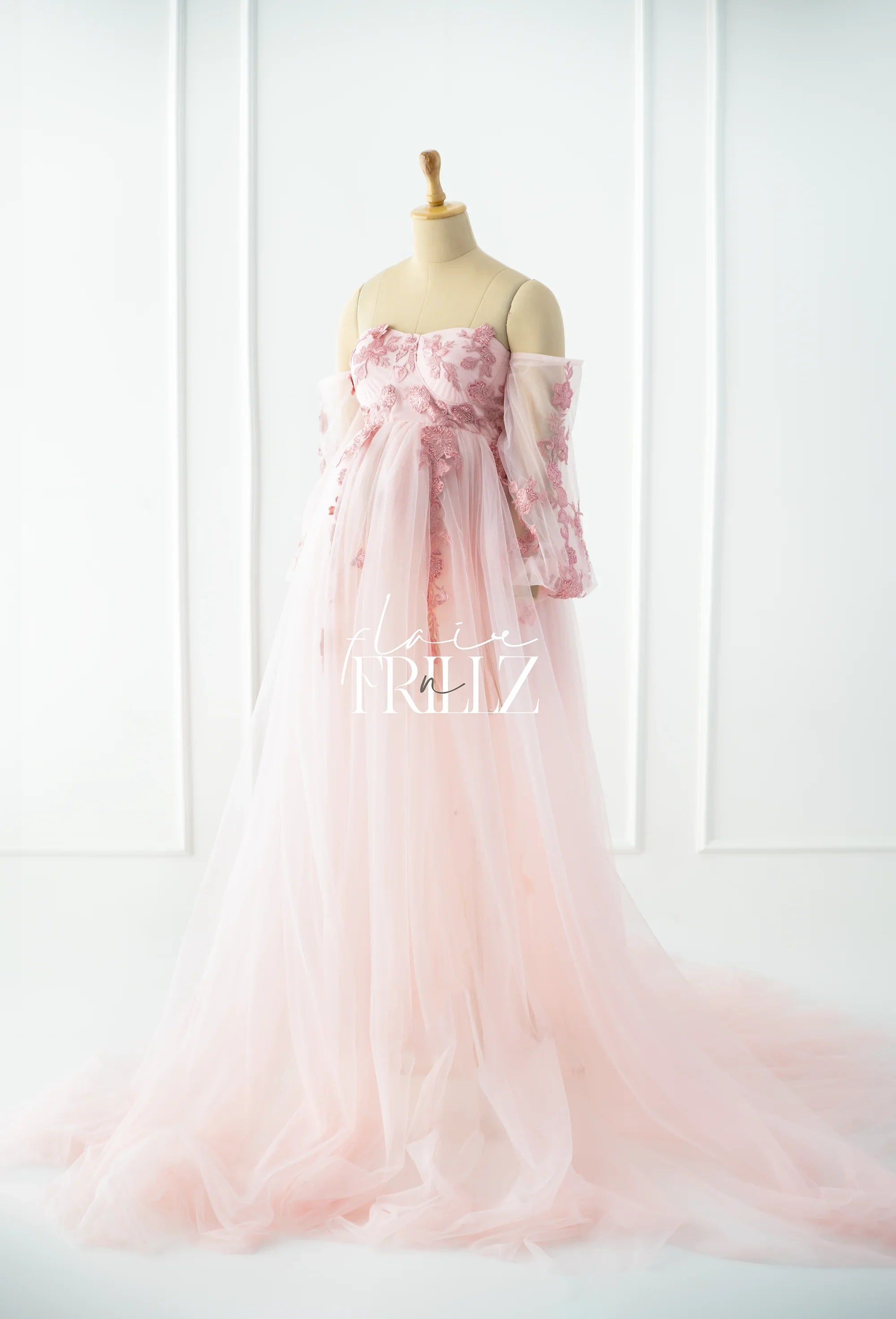 Light pink maternity gown with floral lace bodice and long tulle skirt on mannequin