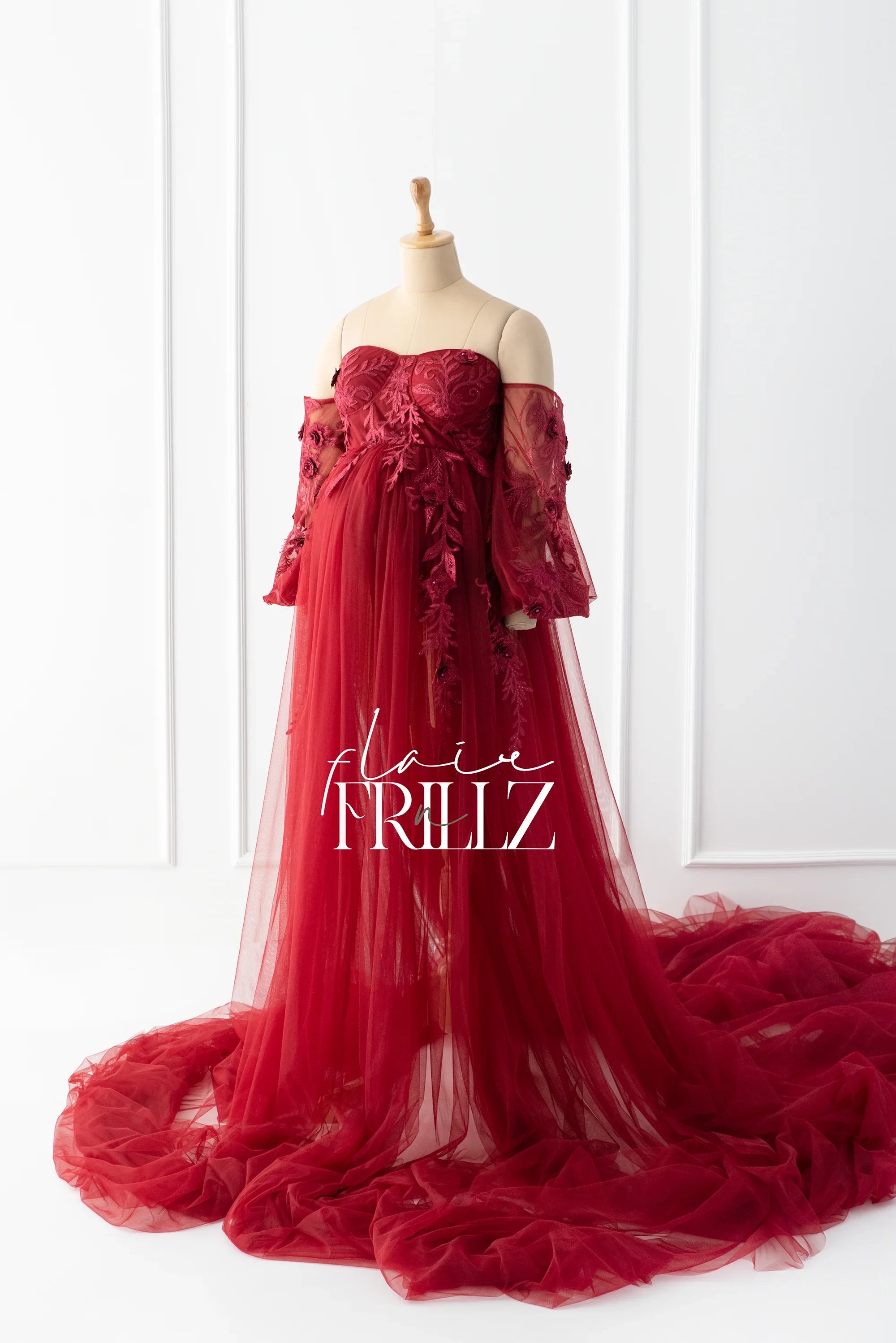 Elegant burgundy off-shoulder maternity gown with lace details and tulle train on mannequin