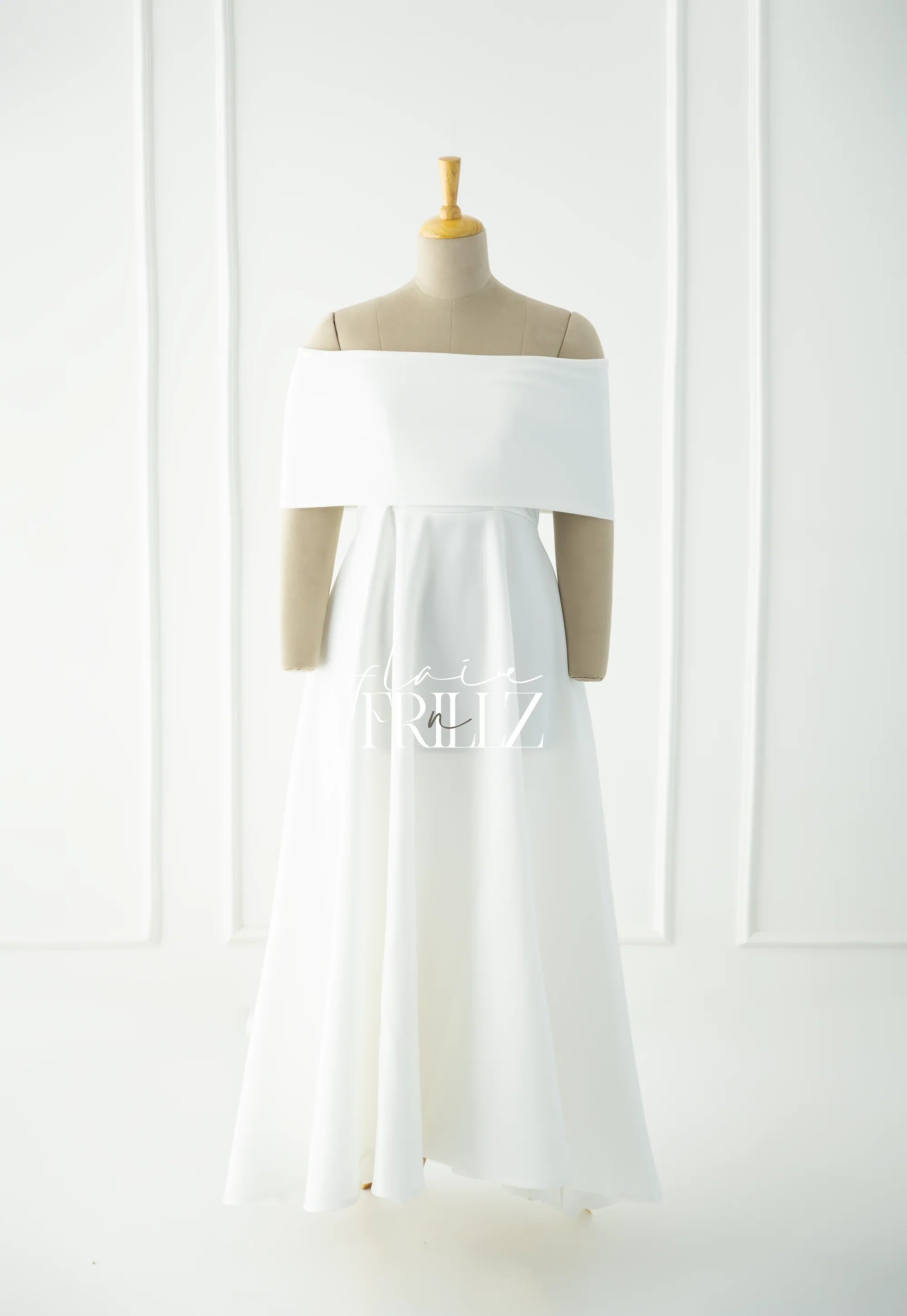 Elegant white off-shoulder maternity gown on mannequin in minimal studio setting