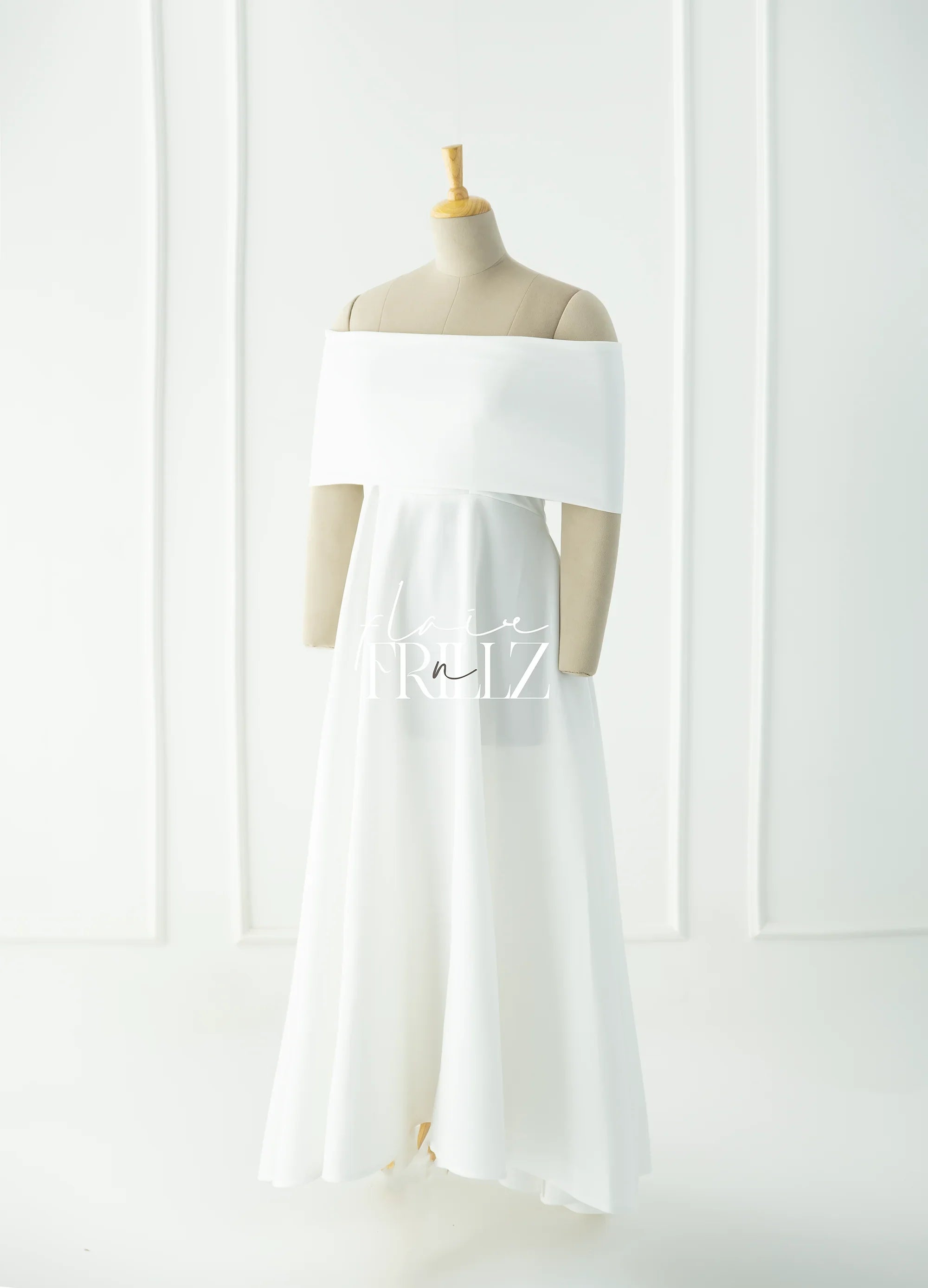 Elegant white off-shoulder maternity gown on a mannequin in a minimal studio setting