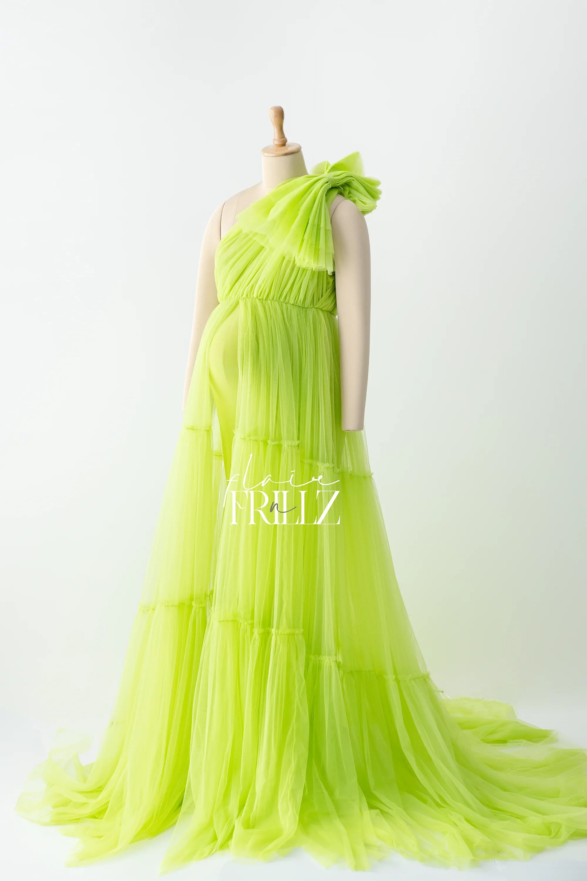 Lime green tulle maternity gown with ruffled one-shoulder design on mannequin