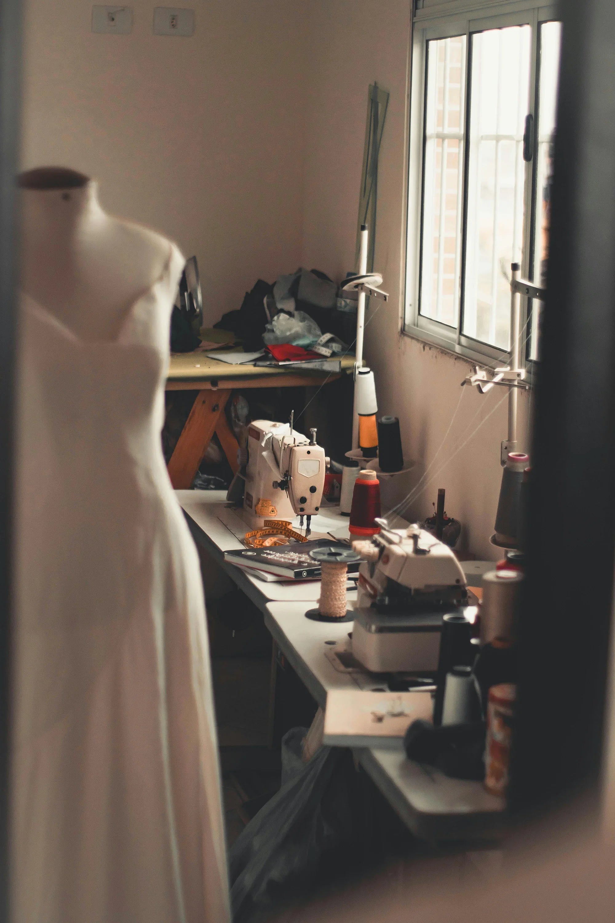 Maternity gown on mannequin in sewing studio with sewing machines, thread spools, and fabric, showcasing handmade comfort and style.