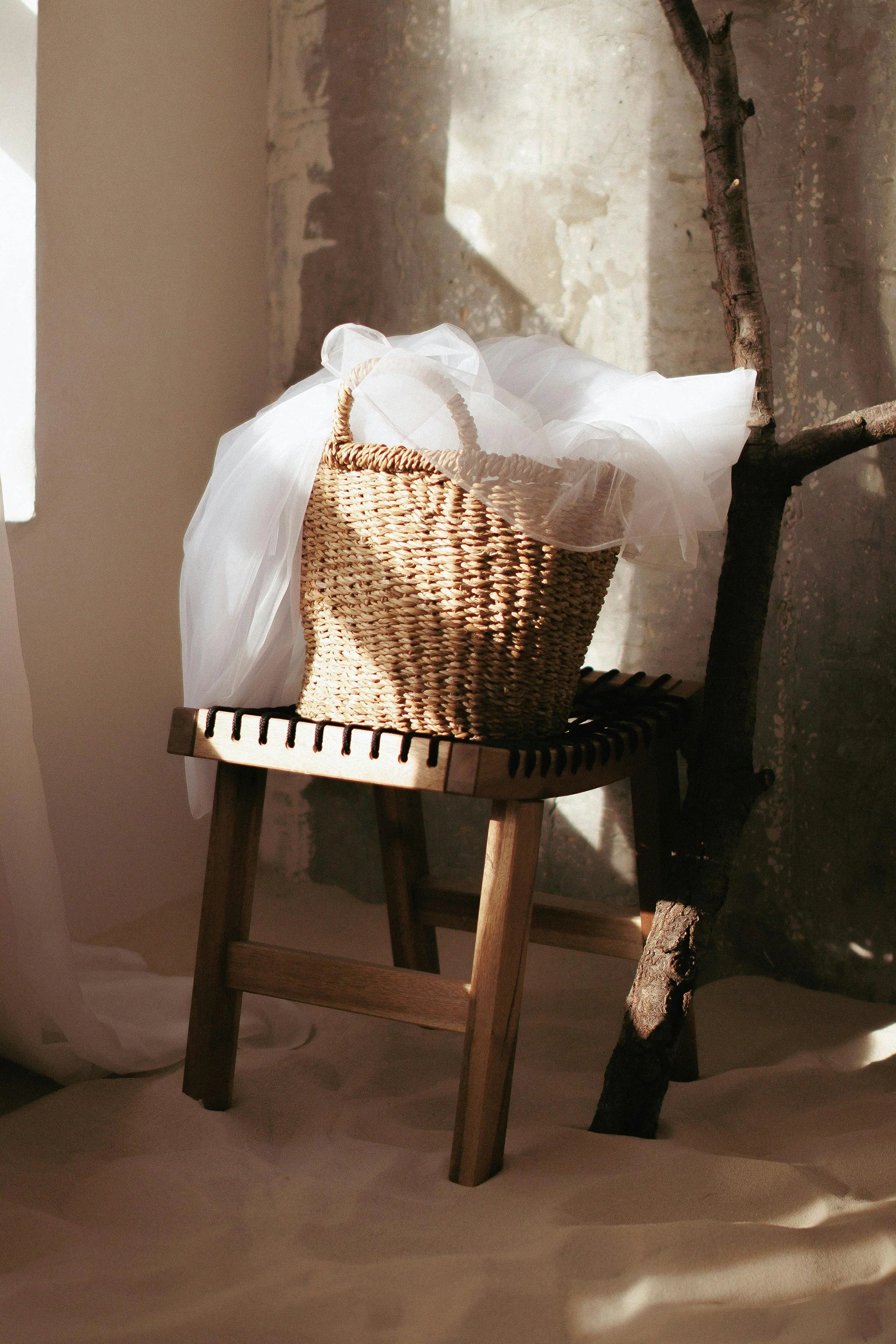 Woven straw basket with white tulle on wooden stool, soft natural light, rustic decor