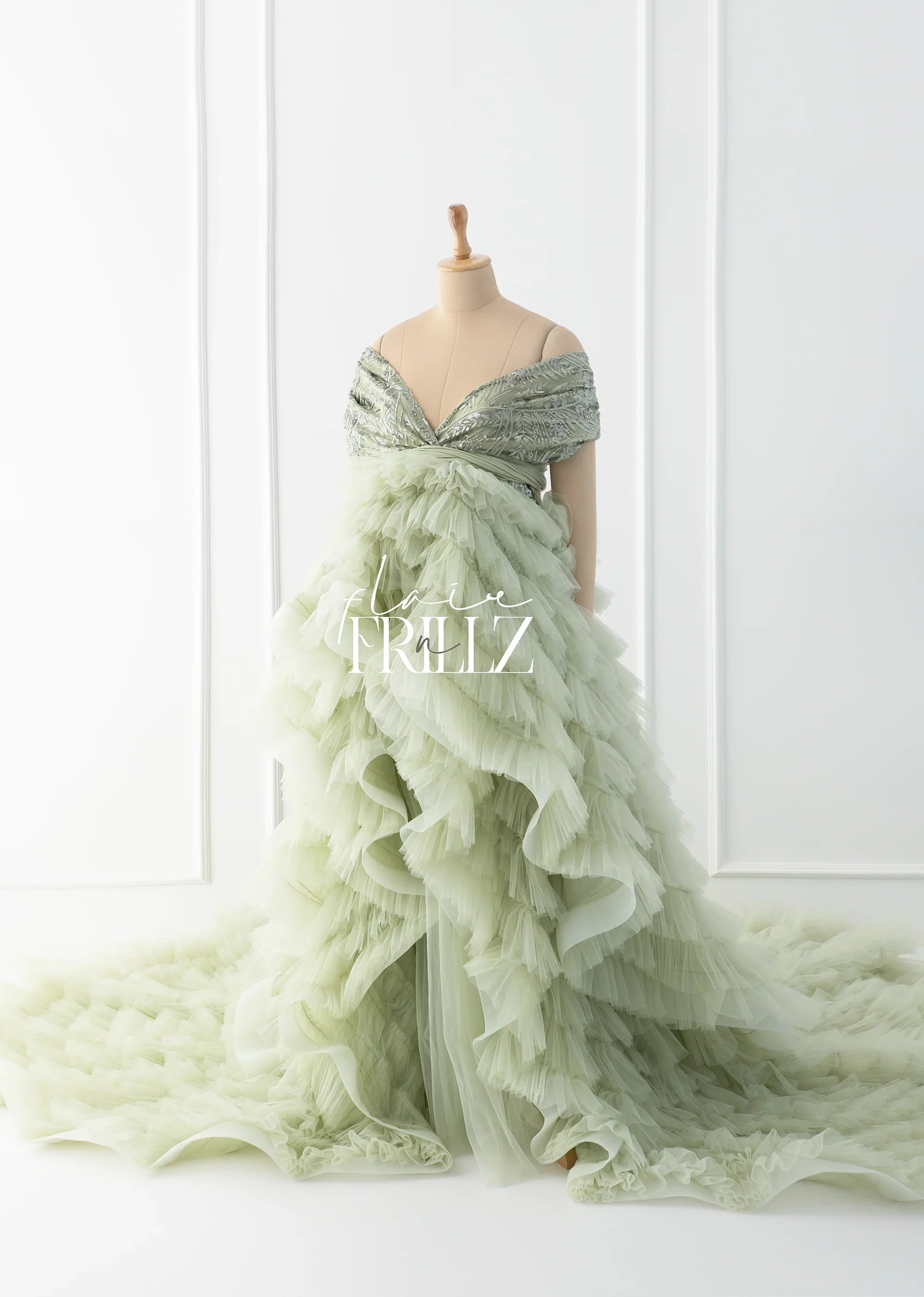 Sage green maternity gown with ruffled tulle layers and off-shoulder sequin bodice on mannequin