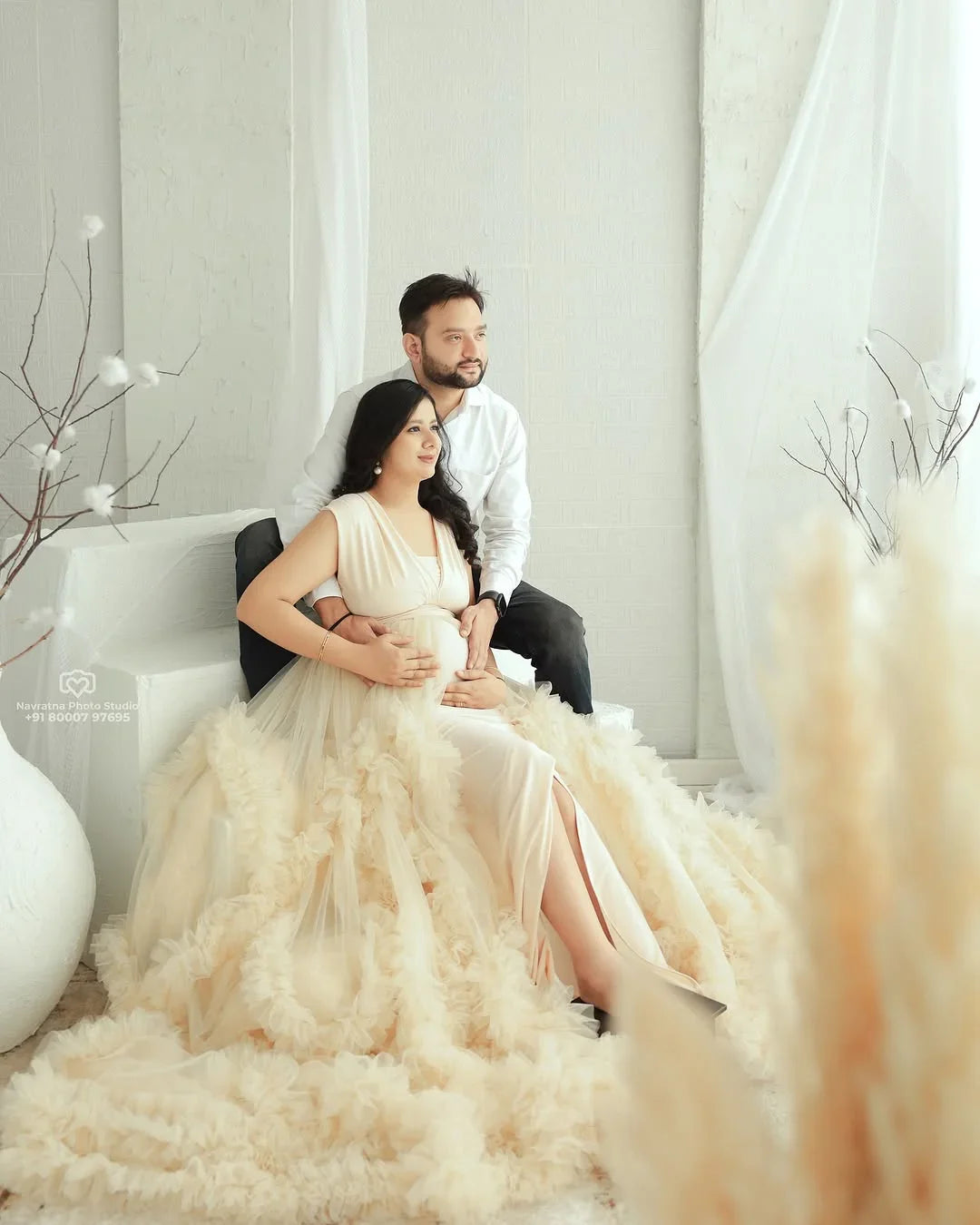 Pregnant woman in elegant beige maternity gown with partner in bright, airy room