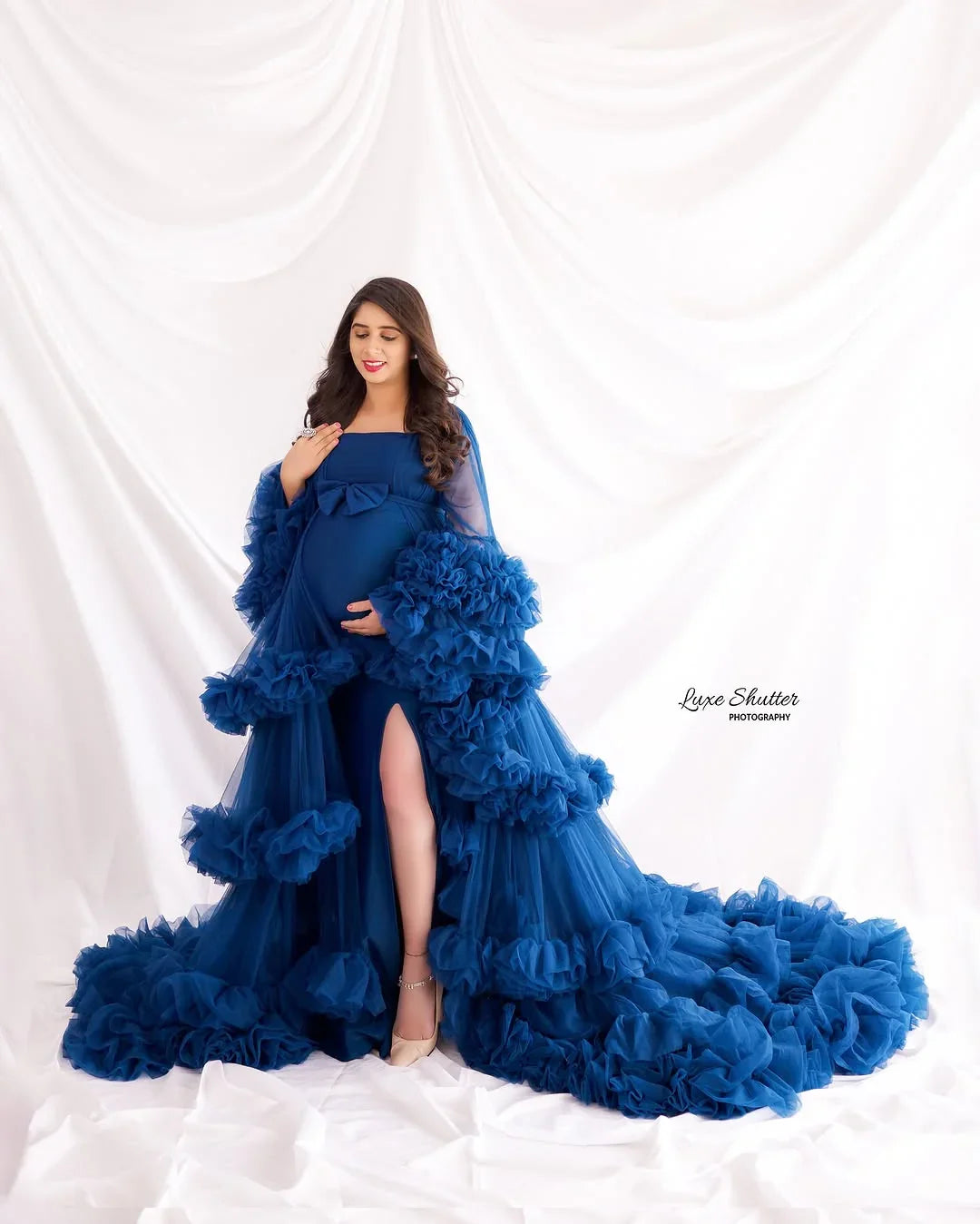 Pregnant woman in elegant blue ruffled maternity gown with long train, posing indoors