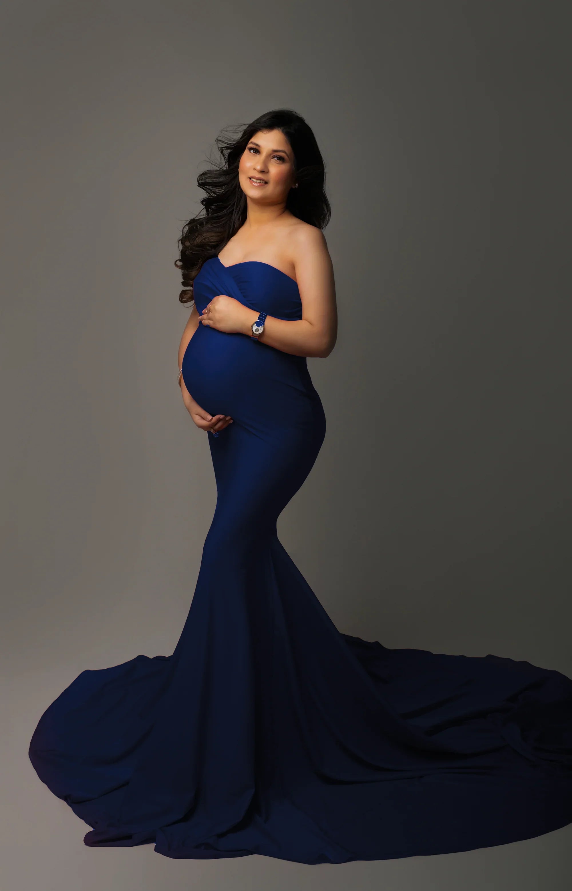 Pregnant woman modeling a strapless royal blue maternity gown with a flowing train