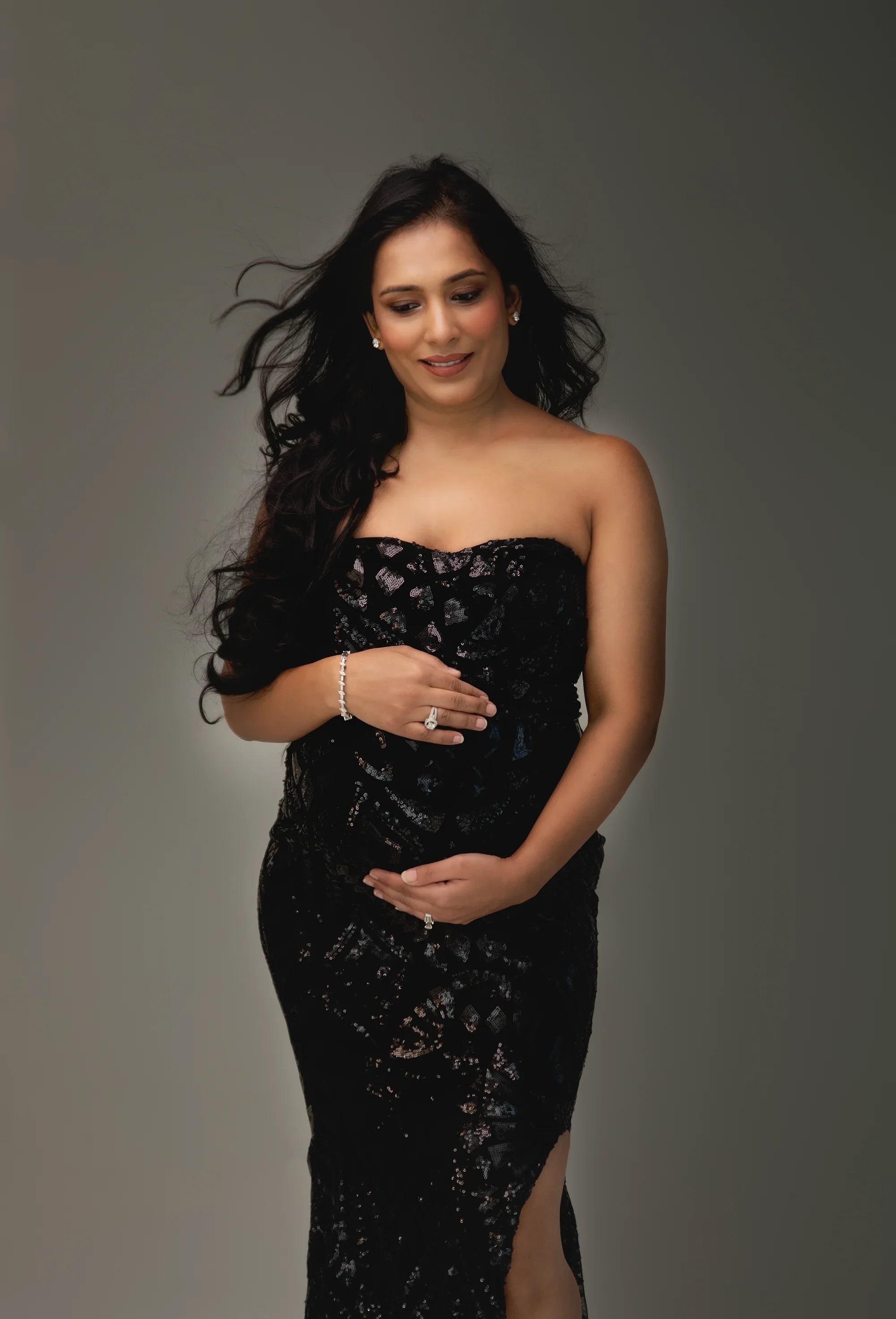 Pregnant woman in a strapless black sequin maternity gown with side slit posing confidently
