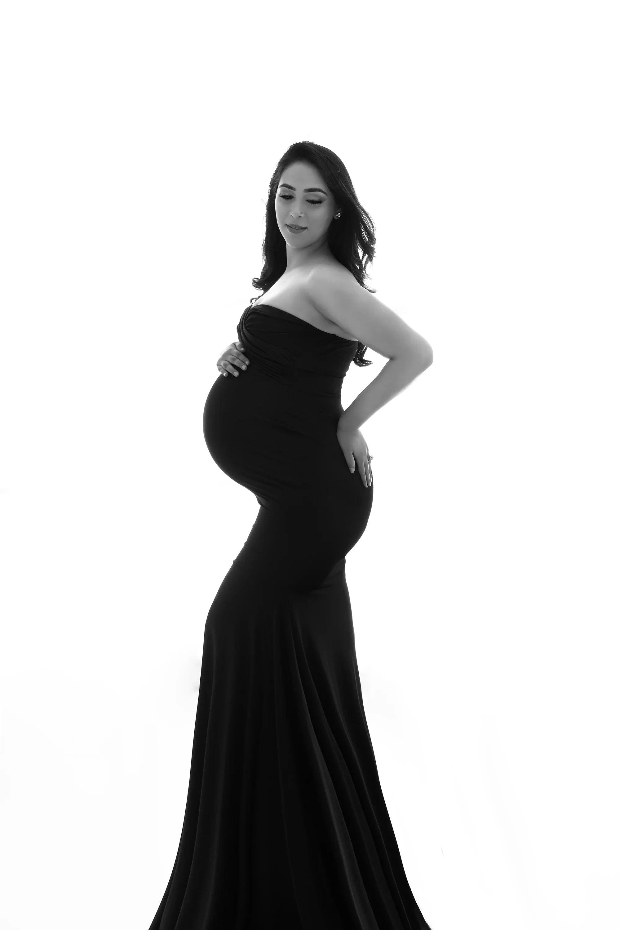 Pregnant woman wearing strapless black maternity gown posing against white background